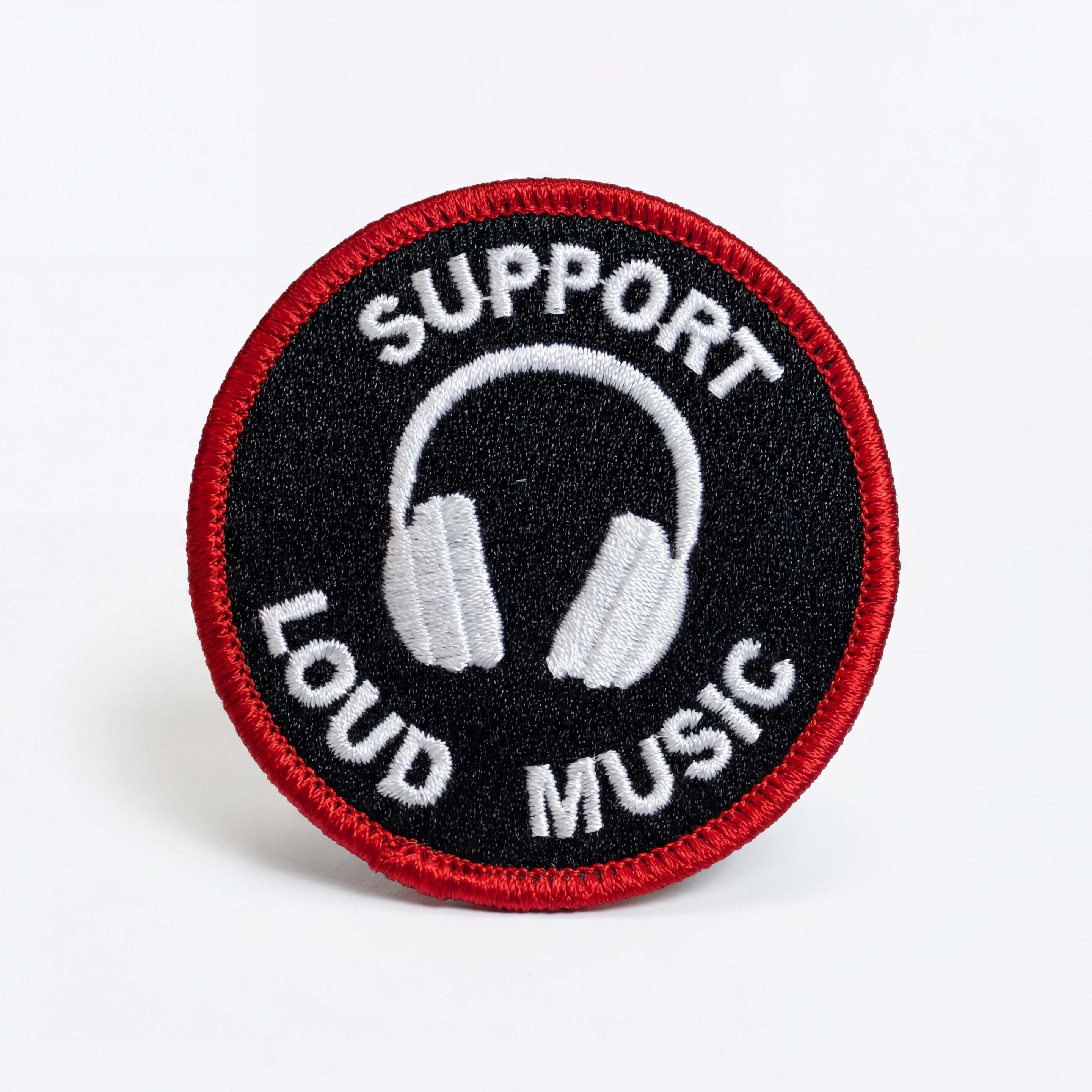 A Black and red round white patch with white headphones in the center that says "support loud music".
