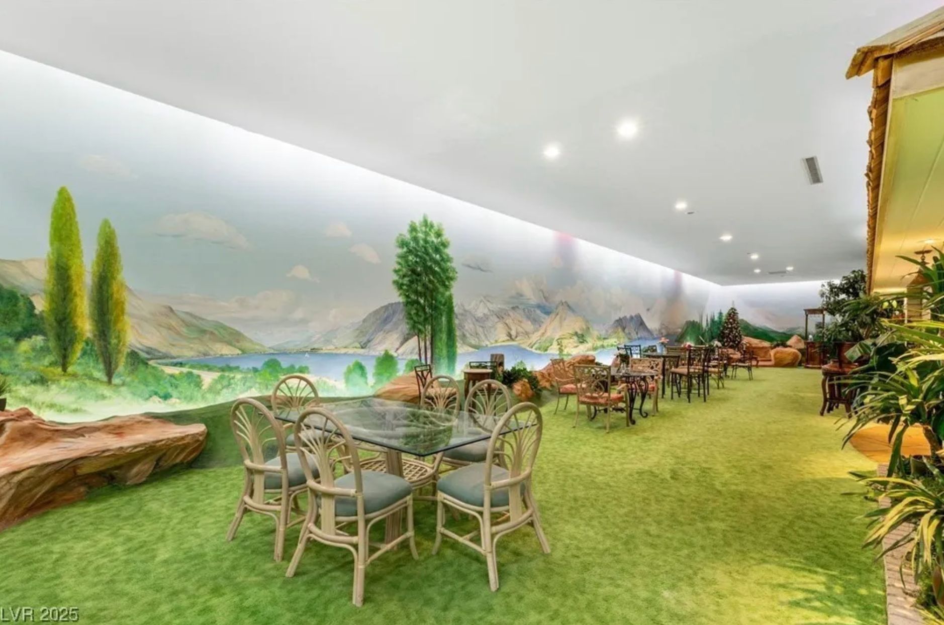 Another view of the underground "yard" showing fake grass, tables with chairs, and a wall with a mural of a landscape. 