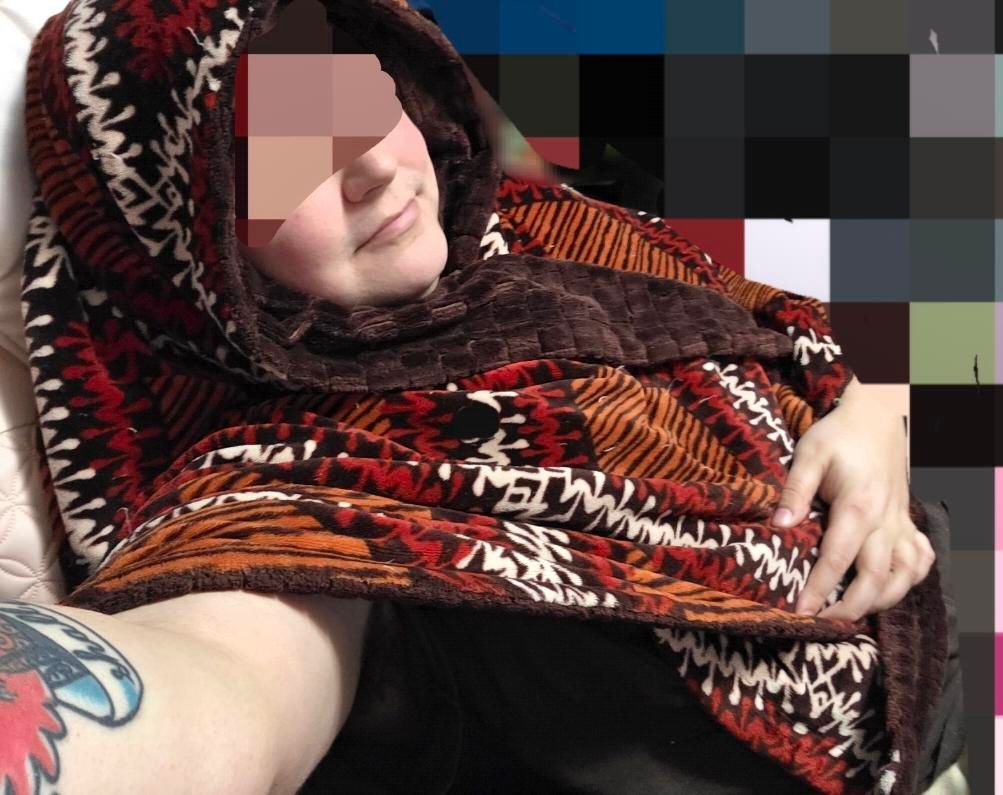 A trans woman sitting leaned back in her chair. A blanket with red and black patterning wrapped around her shoulders. Shes smiling knowing her friends are going to love this picture cause it makes her look like a cute classic older woman wrapped up in a shawl. She is taking the selfie one handed with her forearm just hinting at a tattoo of some sort but it's not clear. This wasn't intended for fedi, but the smile serves the purpose of introducing to new friends just as well.