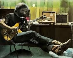 A youngish Jerry Garcia feet propped up and playing a guitar 