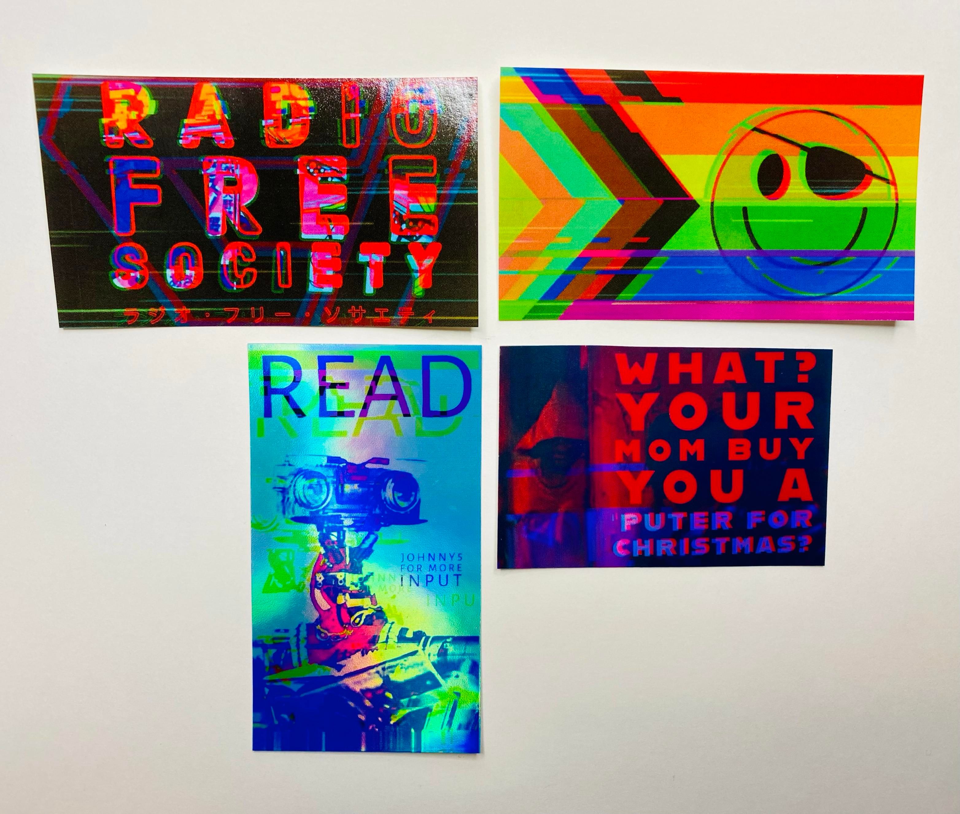 A collection of four colorful stickers on a white background. The designs include the phrases "RADIO FREE SOCIETY," "READ," and "WHAT? YOUR MOM BUY YOU A PUTER FOR CHRISTMAS?" along with a graphic of a smiling face.