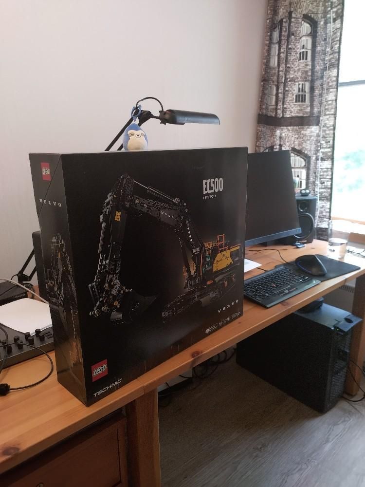 Lego Technics kaivinkoneen paketti työpöydällä. Paketti on niin iso että tietokoneen monitori hukkuu sen taakse.