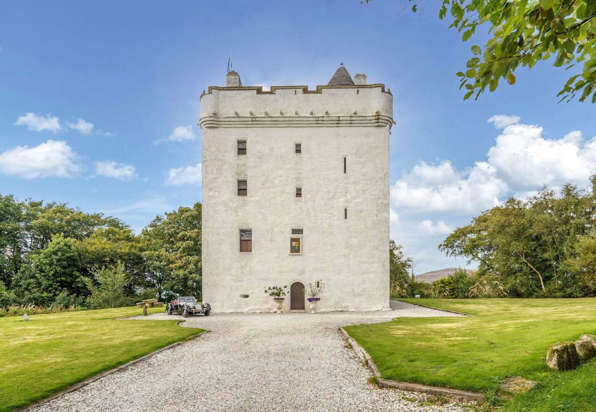 A 5 story medieval style castle that is white/grey in colour with tiny windows, set at the end of a wide gravel covered driveway. 