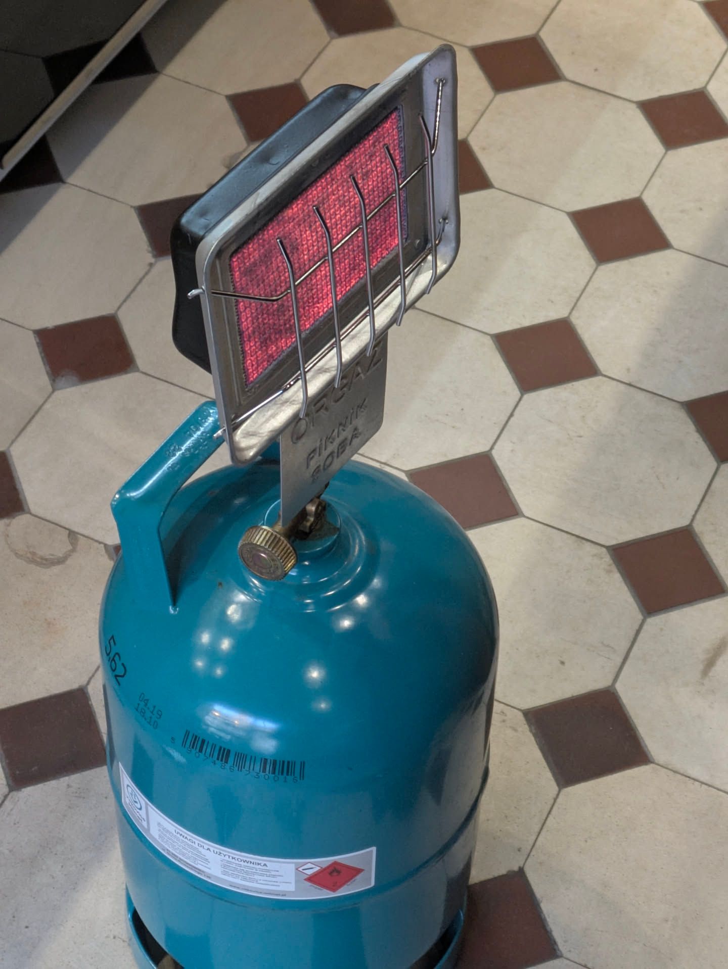 an open flue gas heater head attached to a dark cyan propane tank