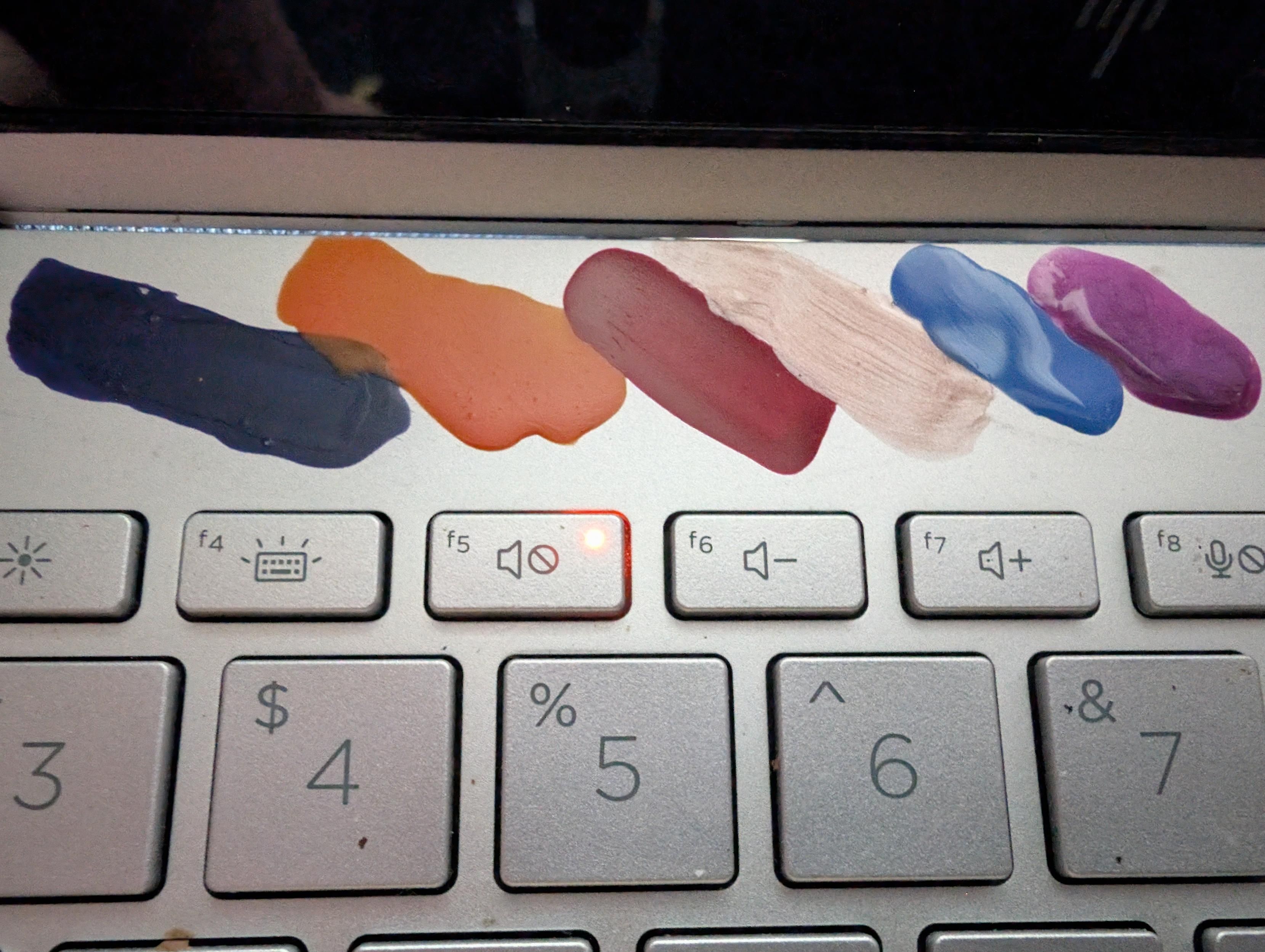 A image of the top of a keyboard with 6 different nail polish colours 

Purple dark, orange, red, dusty pink, blue and purple