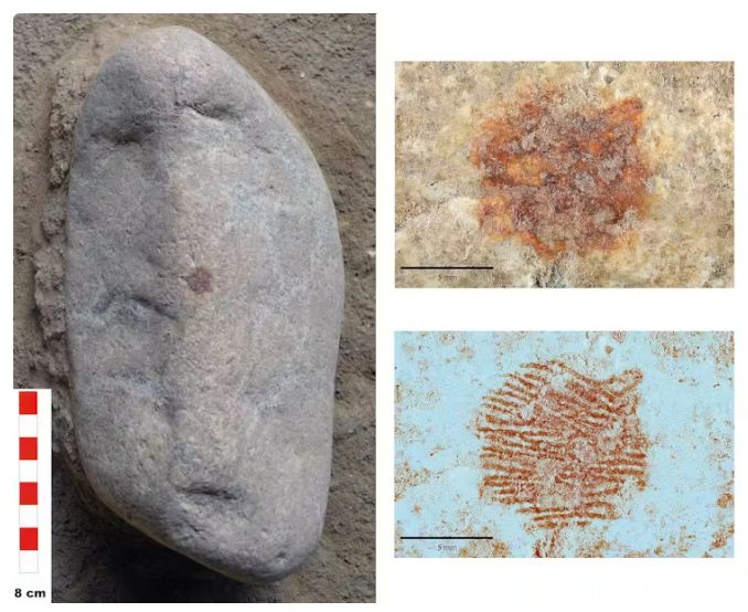 Rock shaped like a human face. It is a long oval. At the top are two depressions that look like eyes and at the bottom is one that looks like a mouth. An ochre dot has been placed right in the center like a nose. On the right are two images of the dot. One is how it looks in reality, a reddish smidge. The second is how it looks on a scan, and the whorls of a fingerprint are clearly visible 