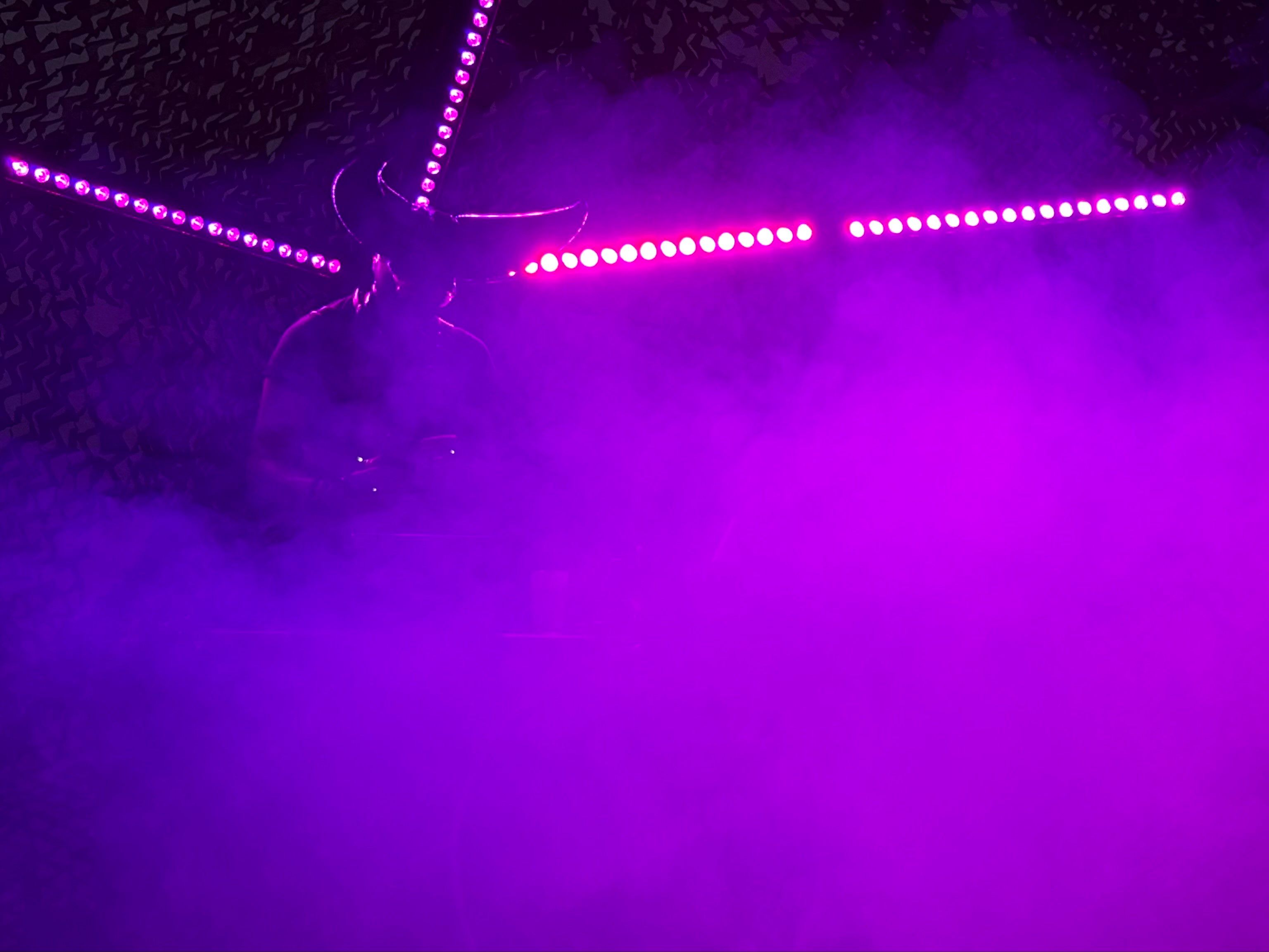 Photo of a DJ wearing a horned mark in an extremely foggy environment. There’s very pink neon lighting illuminating the fog brightly and you can barely see them. It’s tough to capture the vibe of this one for the alt text. 
