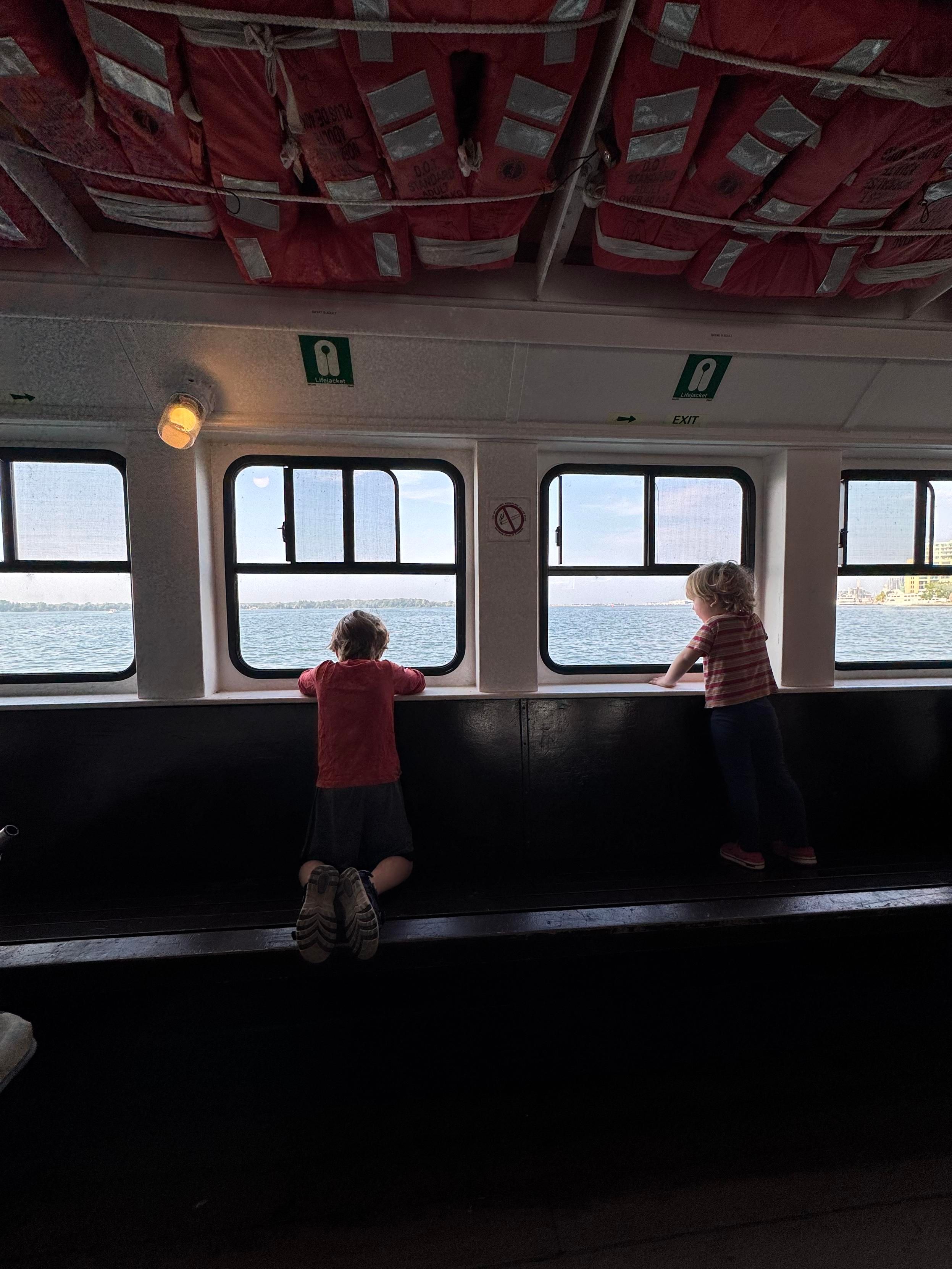 two little kids peering thru the windows of the ward’s island ferry