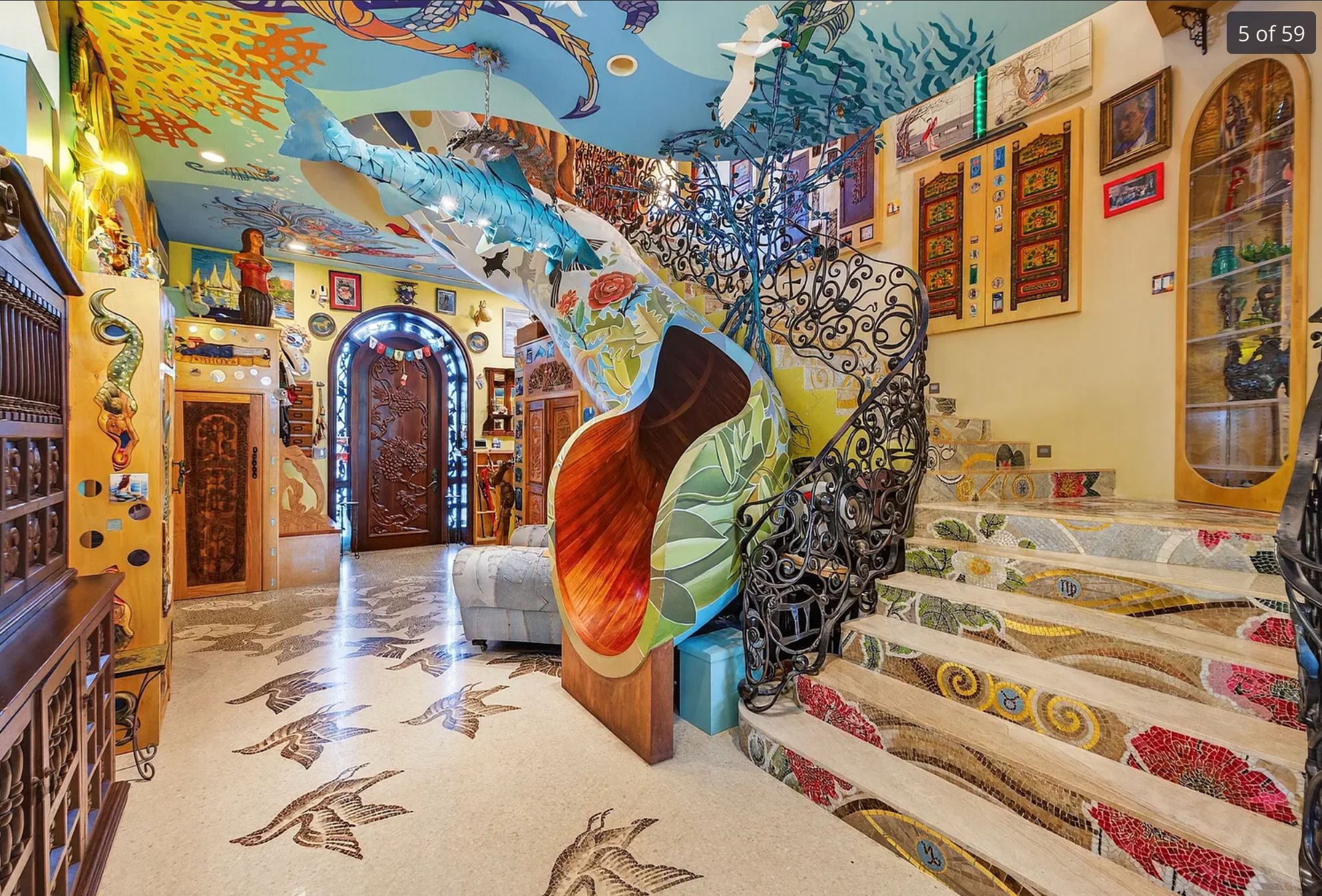 A curving slide next to a stairway, the slide is painted bright colours and has stained timber on the inside.