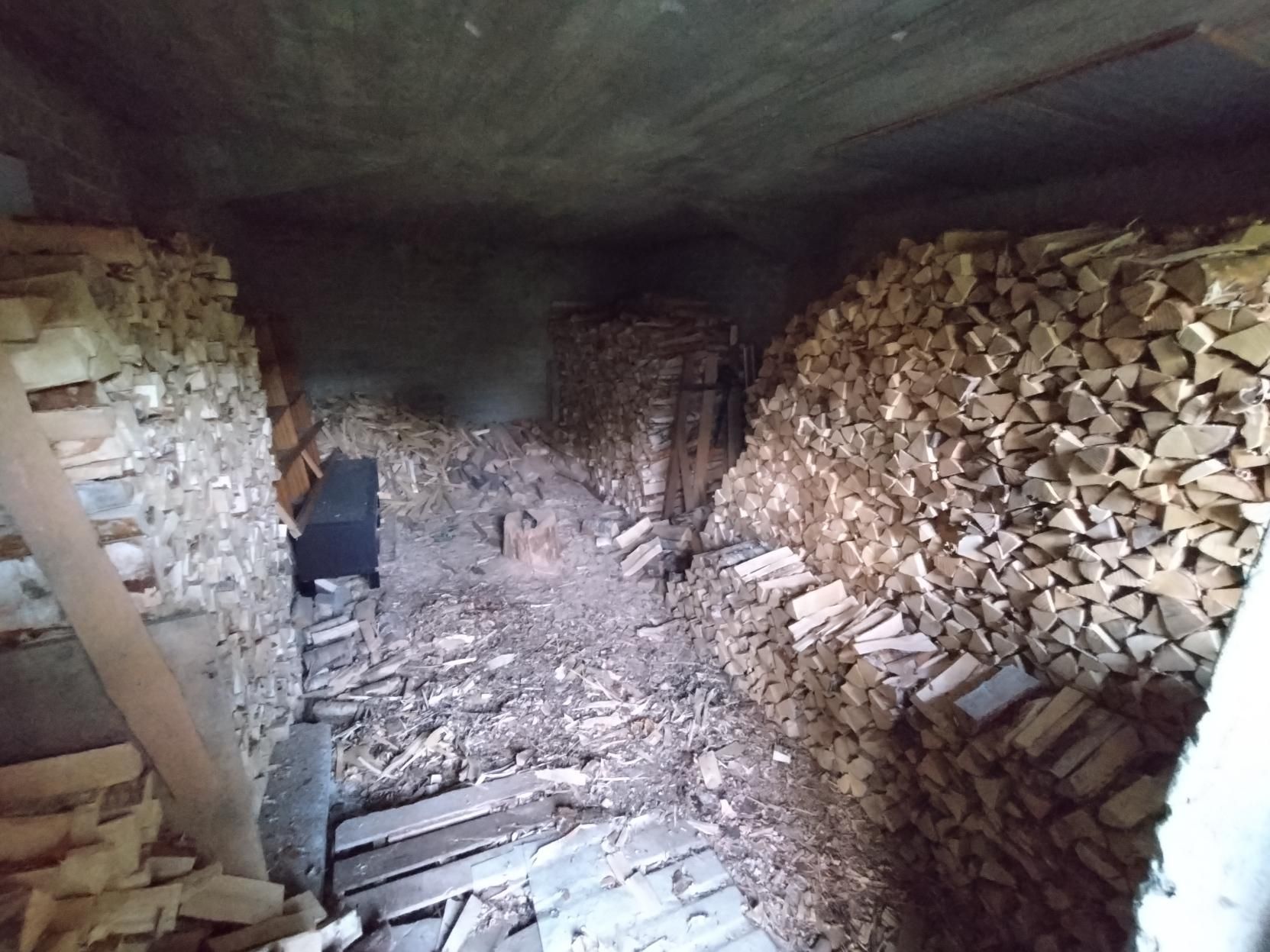 Kuva puuvarastosta, jossa seinien vierustoilla on halkopinoja.