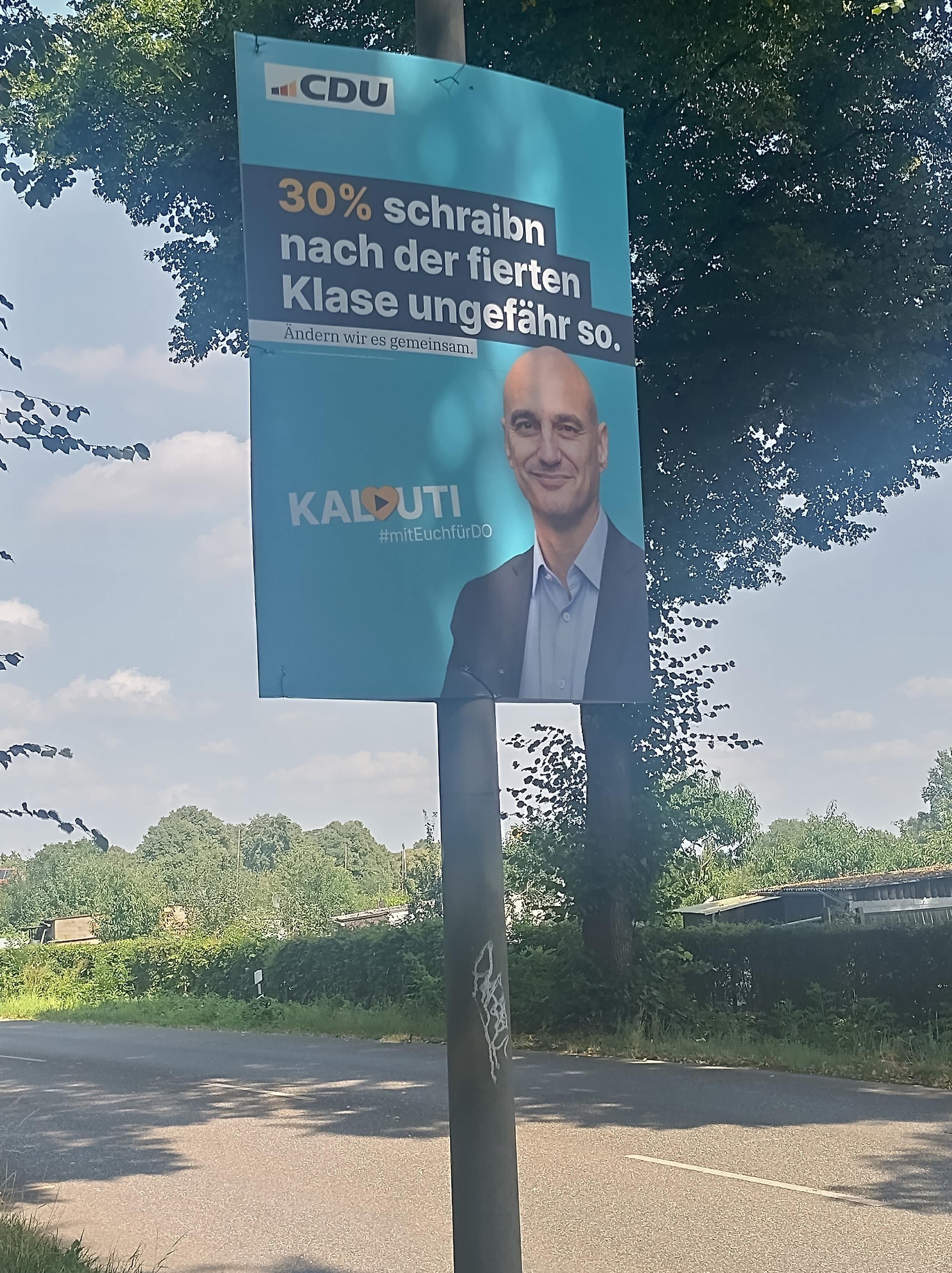 Wahlplakat "30% schraibn nach der fierten Klase ungefähr so" Bild des Kandidaten Kalouti, weißer Mann mit Glatze