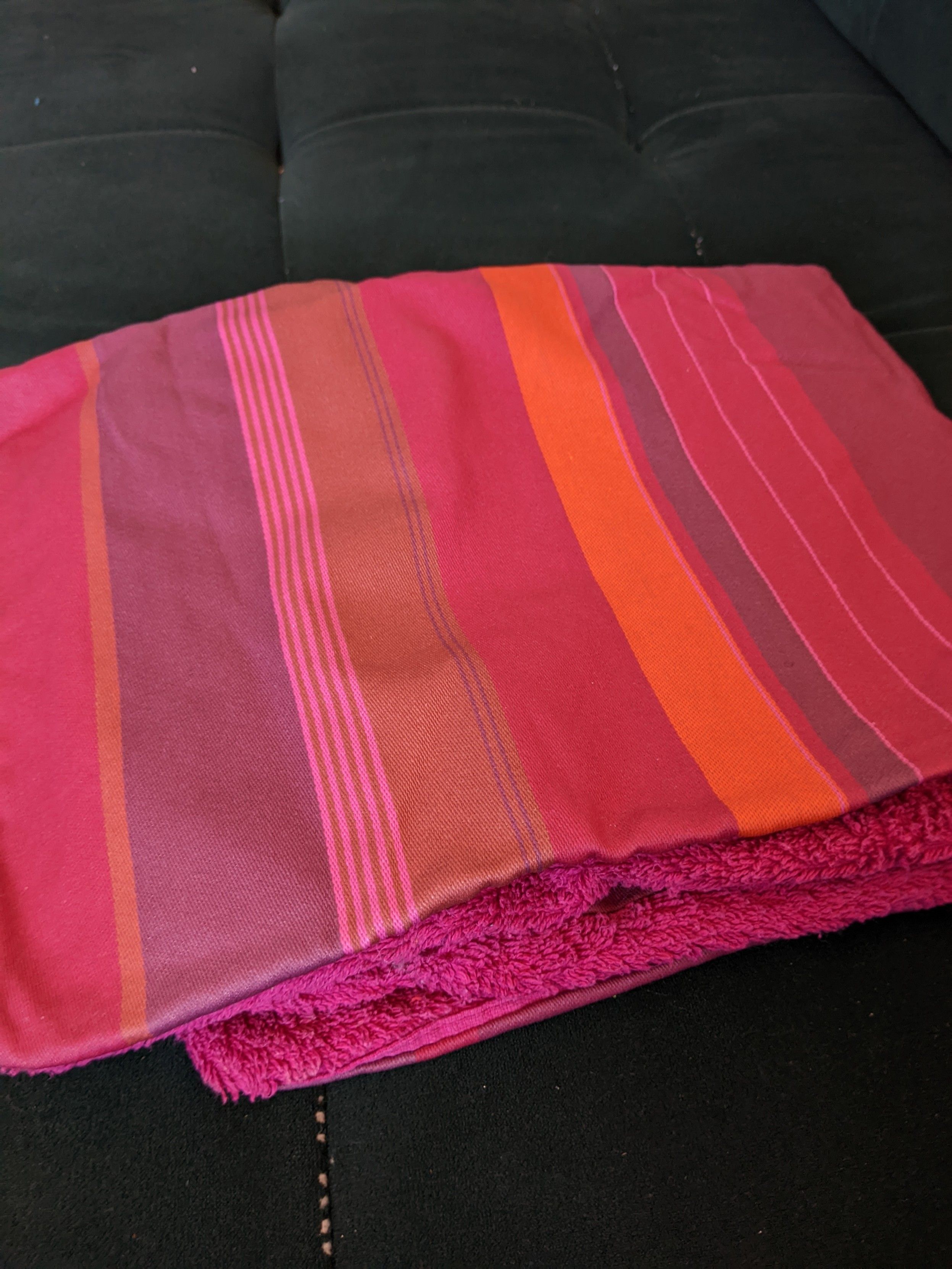 Tapis de change pour bébé : une face coton éponge fushia, une face coton enduit avec des rayures de différentes largeurs dans des couleurs rose/rouge/orange
