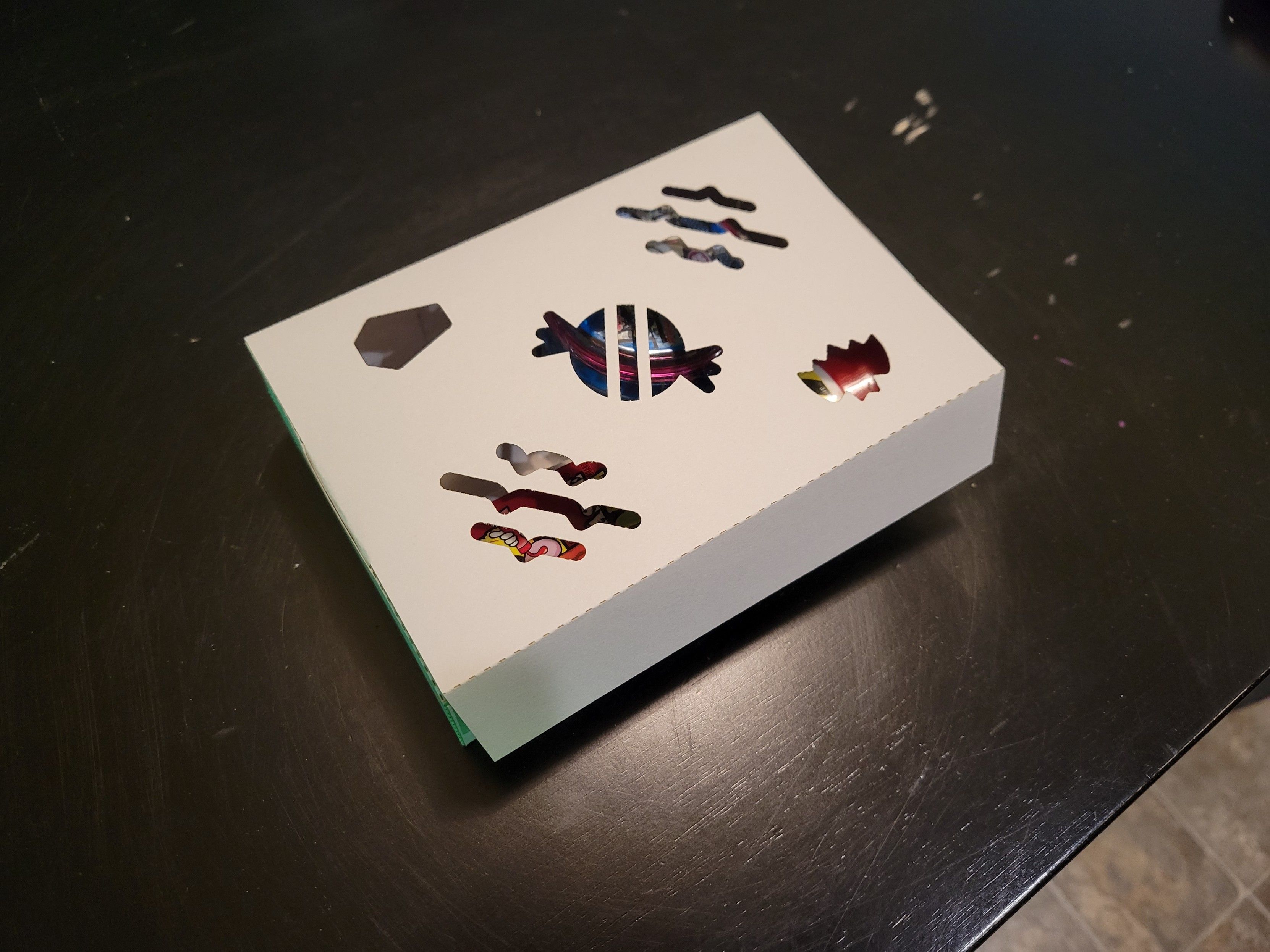 An small assembled box made from laser-cut cardstock featuring Halloween-themed cut-outs in the lid from Font Awesome. There's some candy inside visible through the cut-outs.