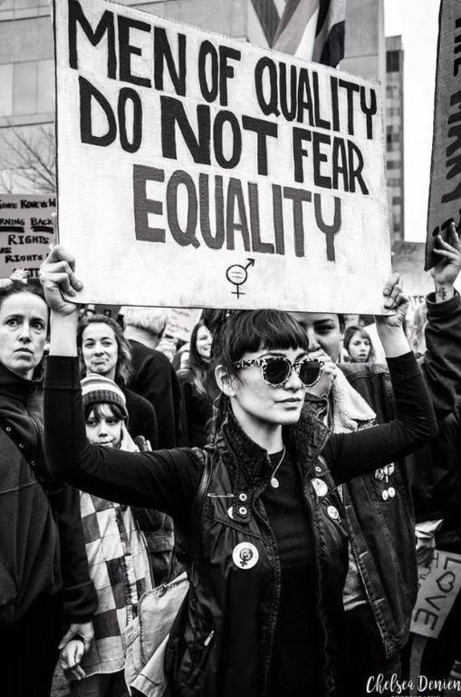 A woman holding a sign reading "men of quality do not fear equality"