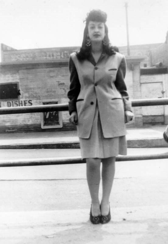 Young woman in a suit with long jacket standing on a street posing for the camera.