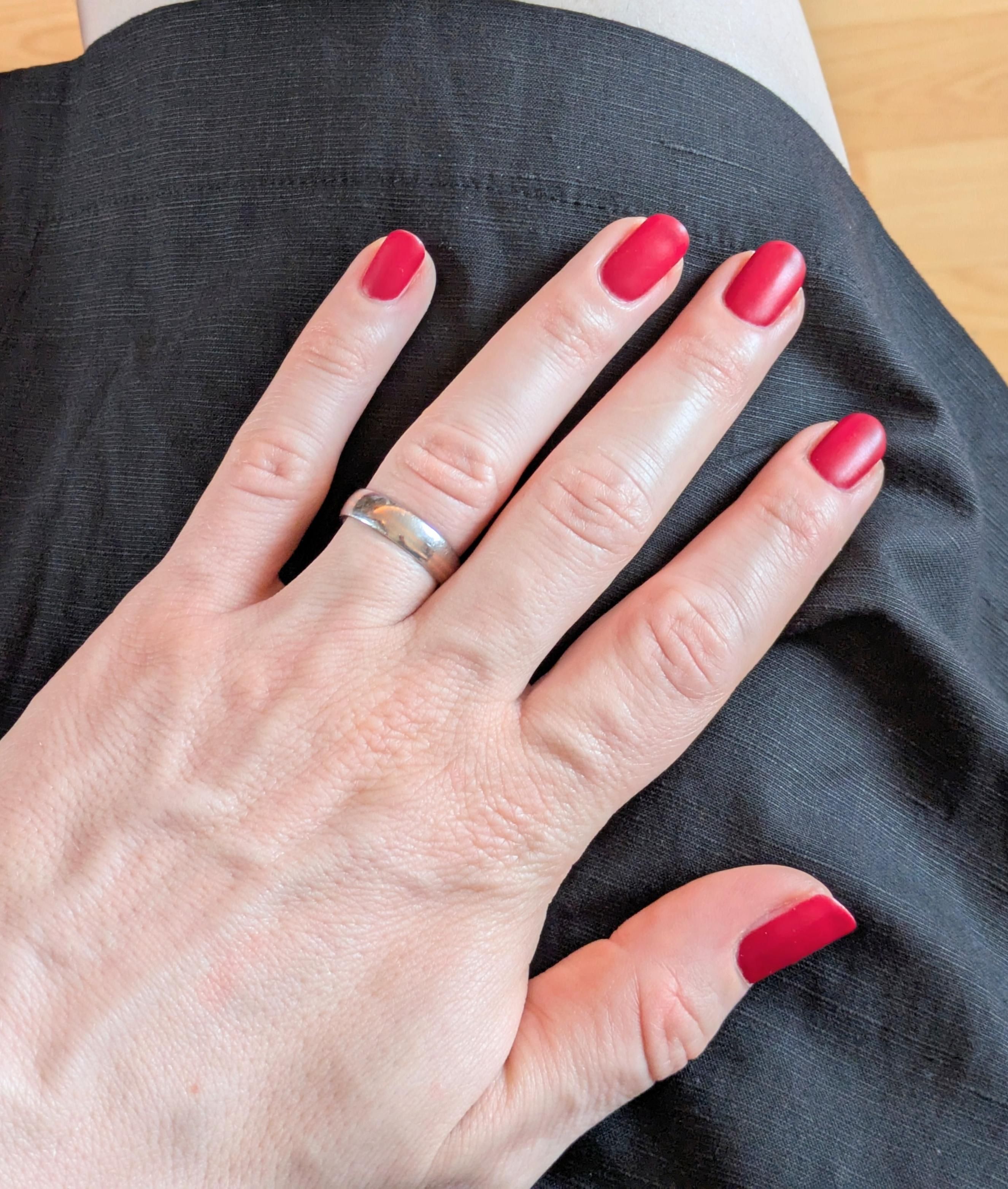A hand with quite bright red nails (mate surface) on a black short skirt. A bit of leg visible.