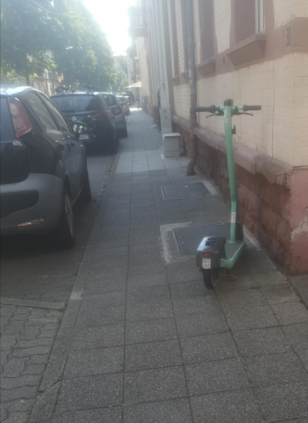 Der selbe Gehweg wenige Meter weiter, ein abgestellter E-Scooter nimmt ca. ein Viertel des Querschnitts ein. 