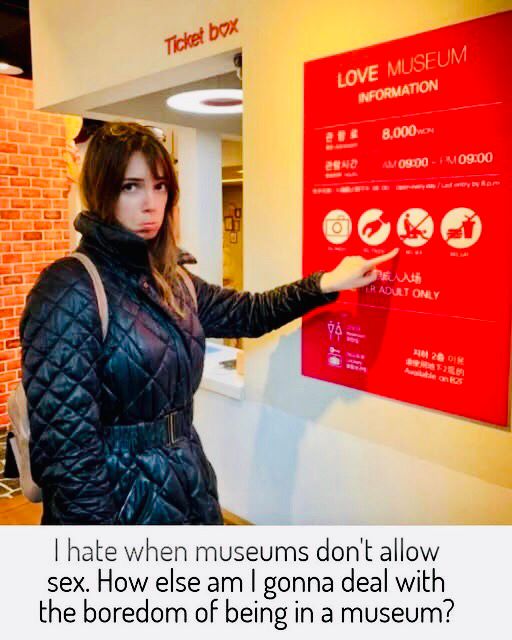 woman pouting as she looks at the camera, pointing to a sign in the love museum depicting “no sex” and doggy-style is crossed out explicitly 