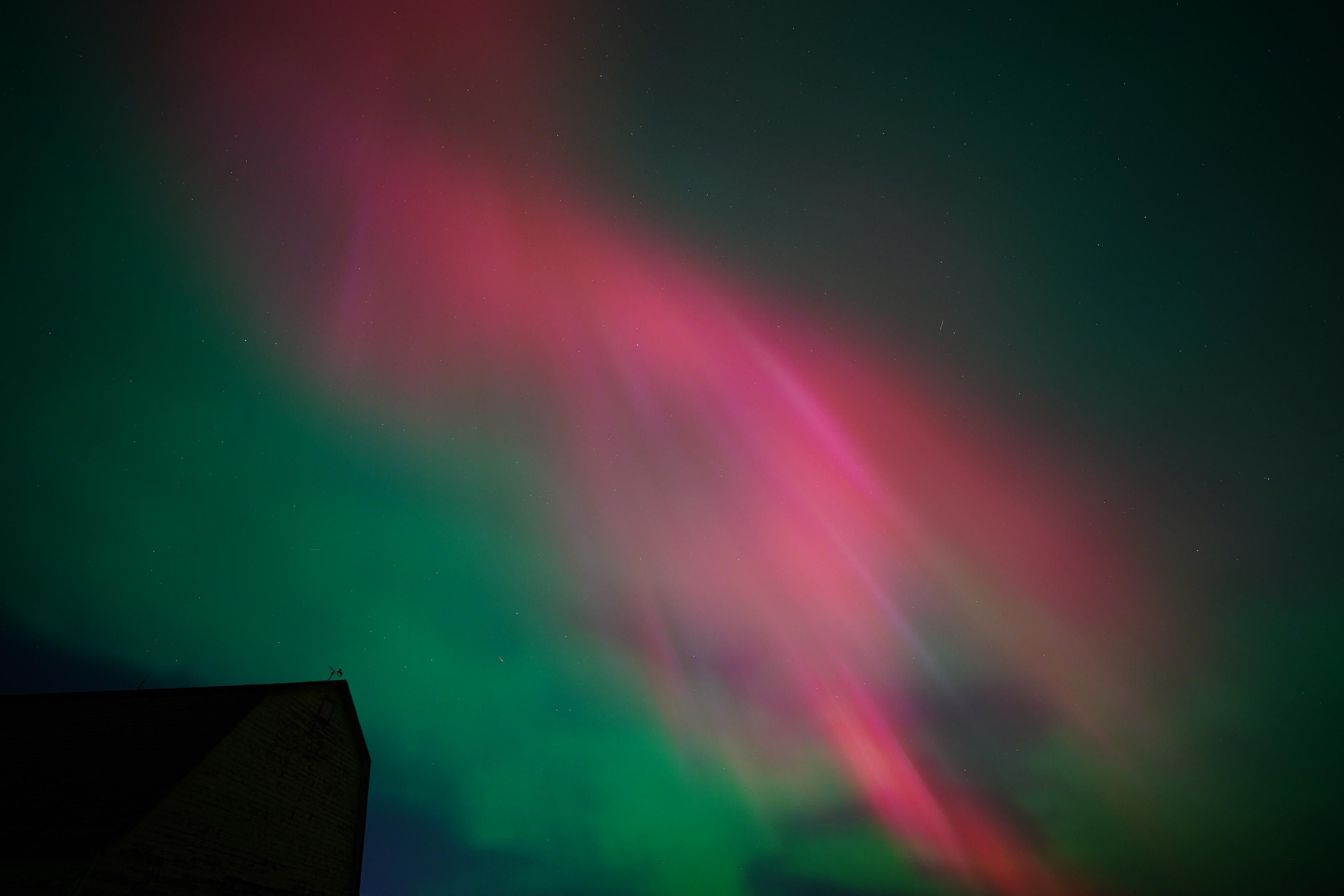 Bright red aurora with pillars mixed in, and some green around the edges.  There's the silhouette of an old barn in the bottom of the photo, including an old weather vane. 