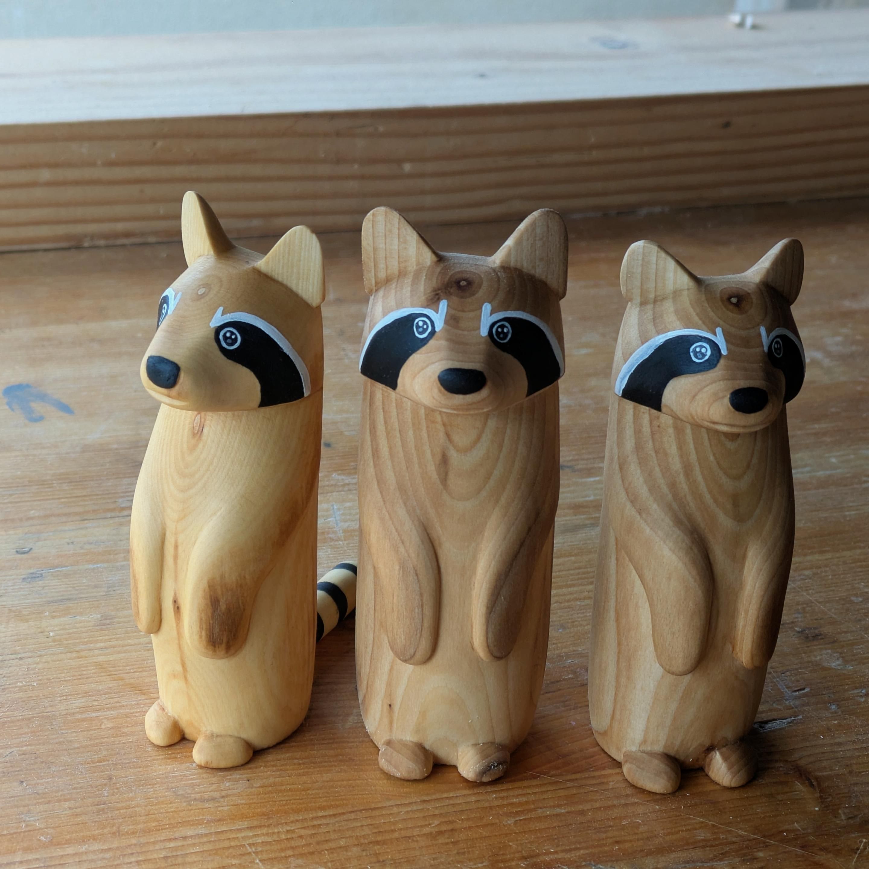 3 woodcarved standing raccoon on a workbench