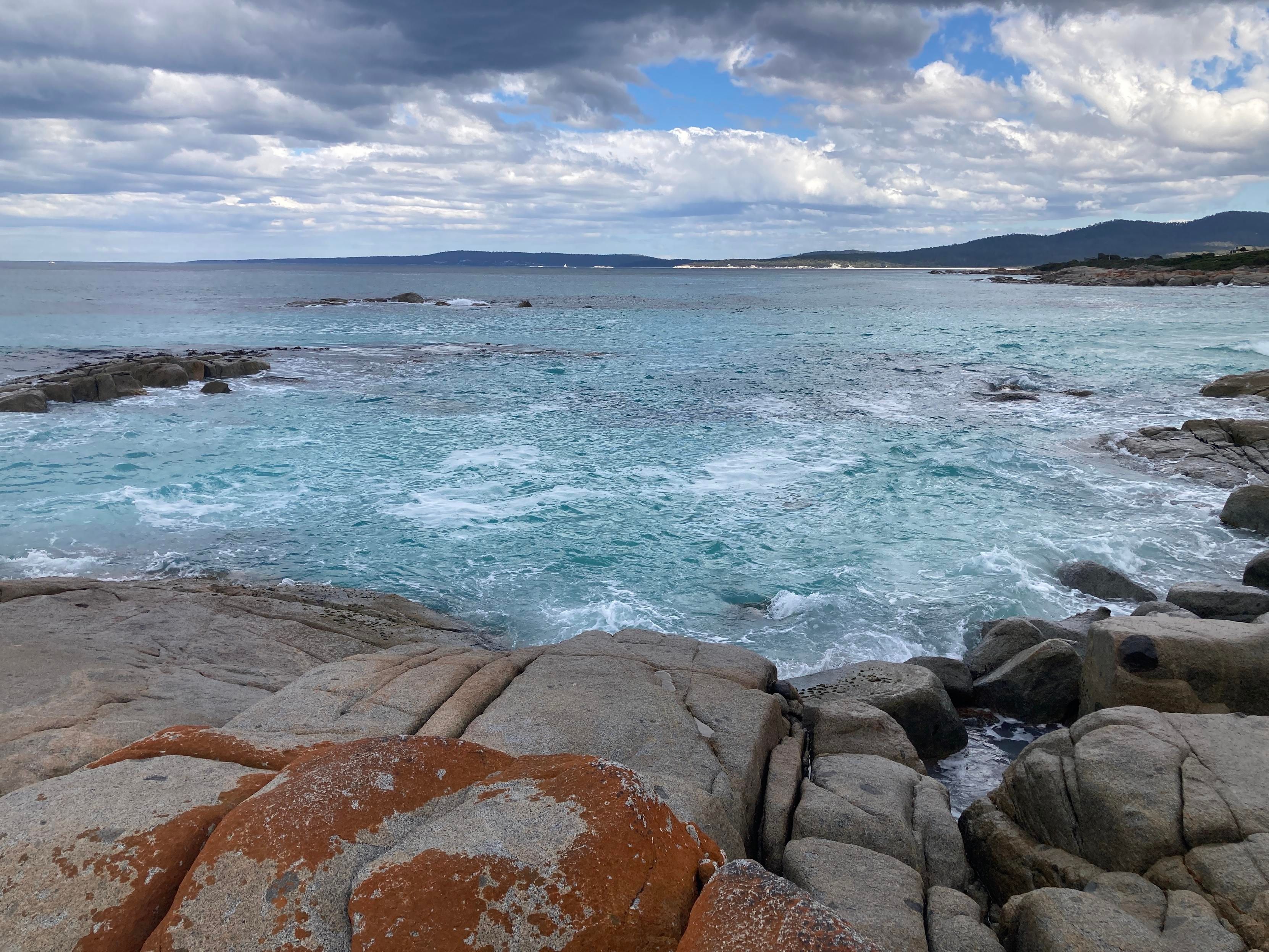 Scenic photograph of an ocean bay on a rocky coast. It shows the bay of fires in Tasmania.