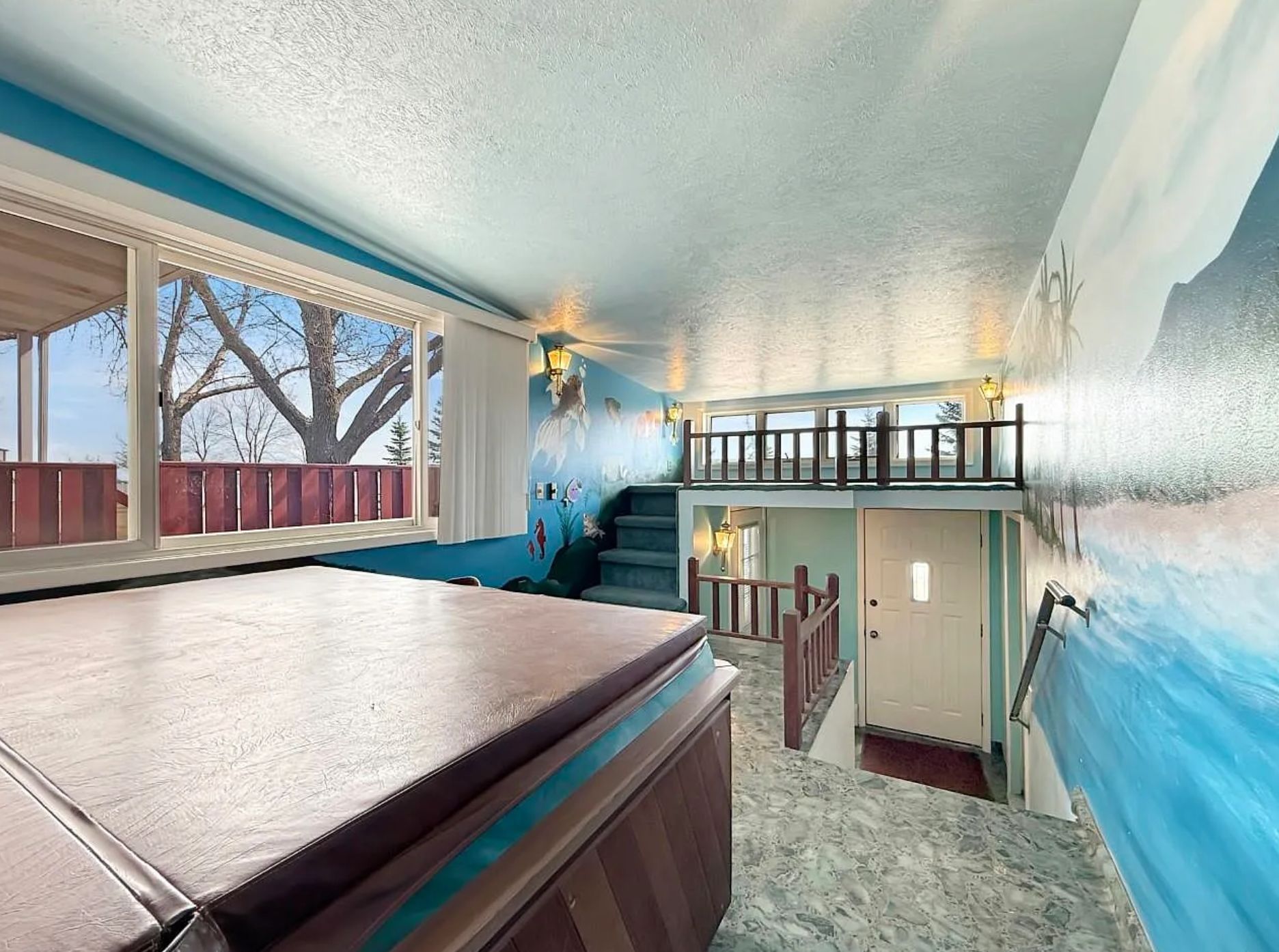 A landing right near the front door that has a hot tub, and at the far end of the area is some stairs going up to a very small platform with nothing on it. There are also murals painted on the wall, with an ocean and mountain scene. 
