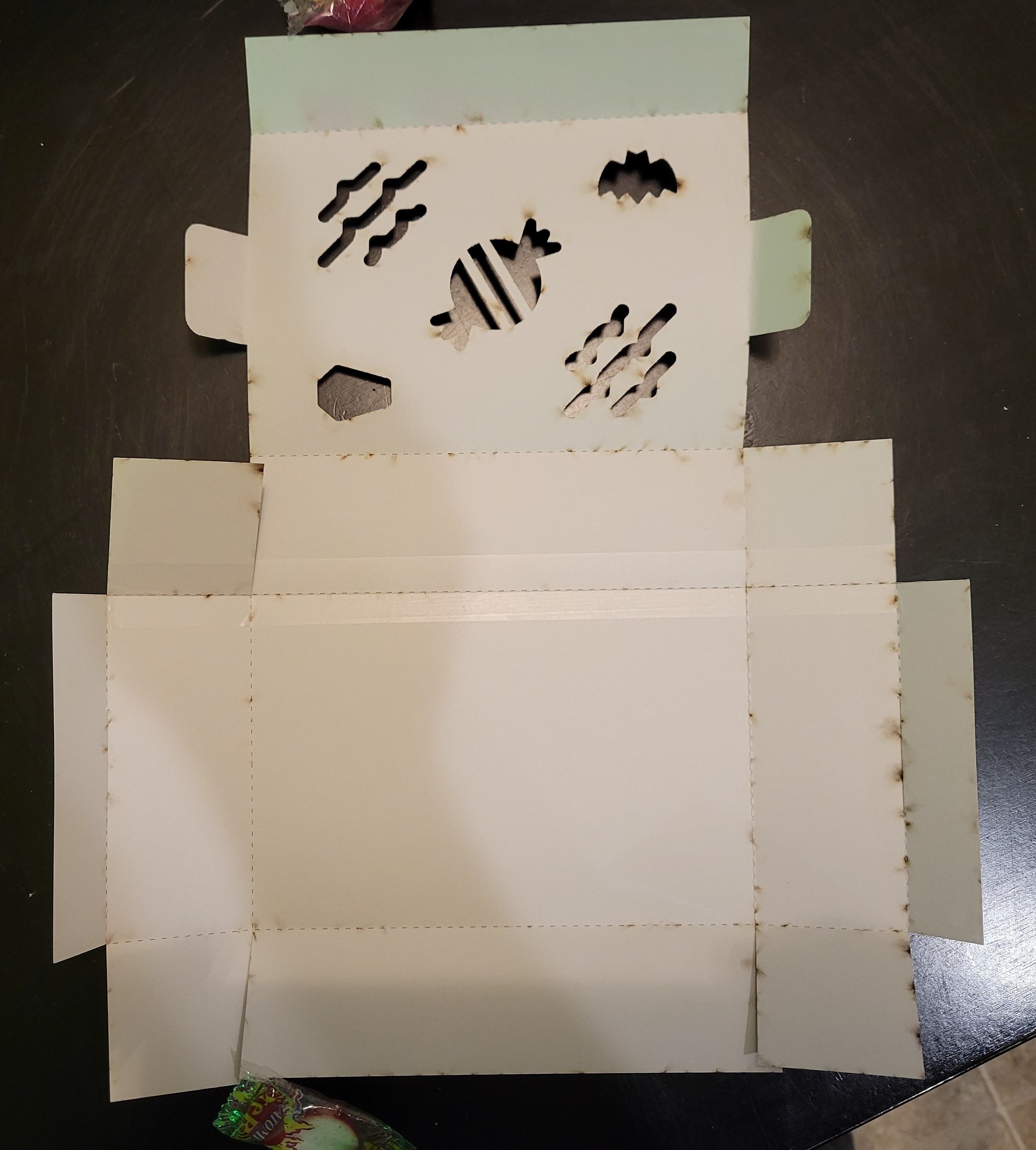 An small unfolded box made from laser-cut cardstock featuring Halloween-themed cut-outs in the lid from Font Awesome.