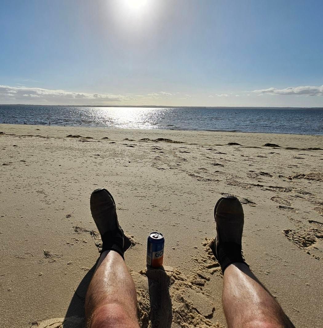 Sitting on the beach after a long ride to the campsite: 40ish km to get from Frankston, then another 5 or so to get to camp from the jetty). My legs are stretched out in front of me, and in between them is a well earned can of beer. The sun is kind of beginning to set, although still quite merciless, and it's reflecting in the water and on the sand.