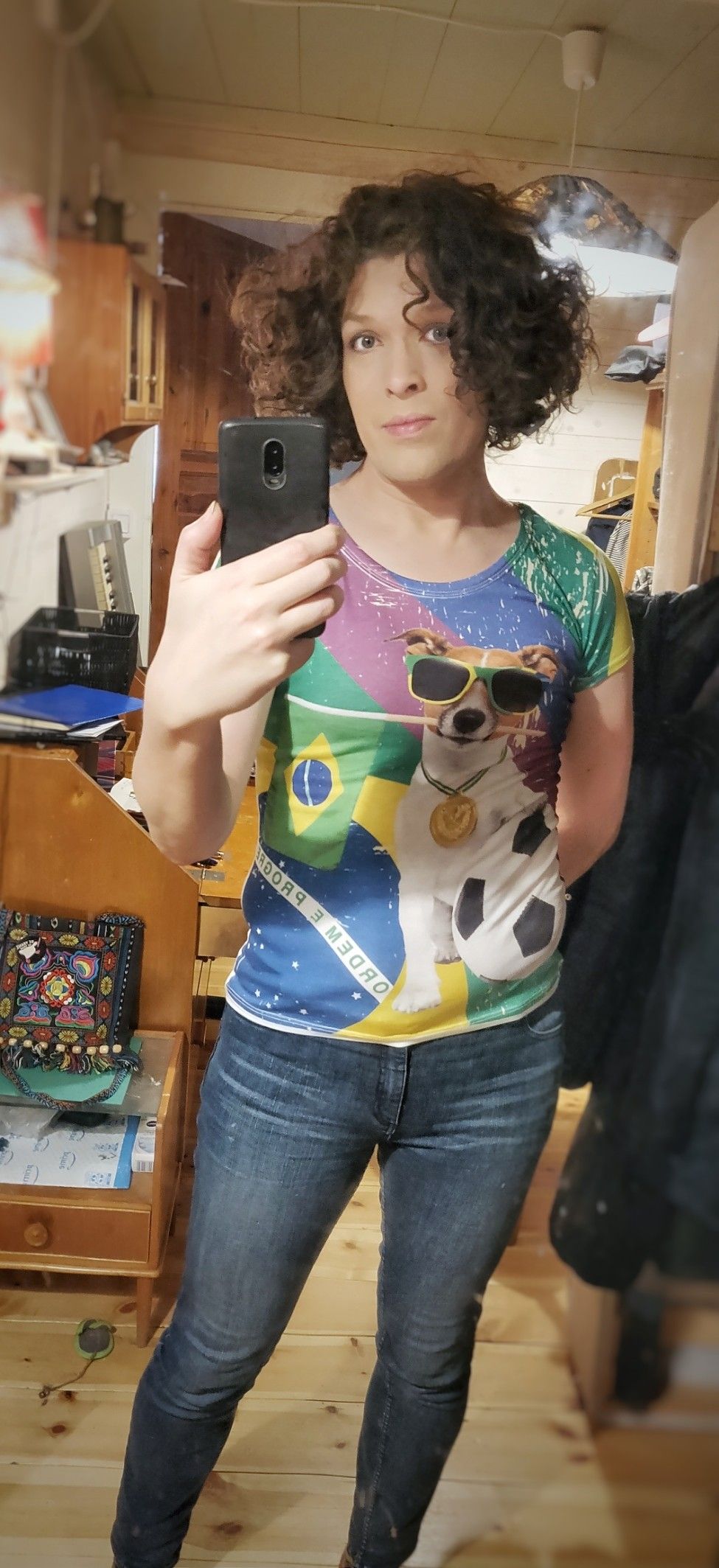 Full-body mirror selfie. I'm wearing tight blue jeans and a colourful tight top with a dog in sunglasses on it. There's also the Brazilian flag for some reason. Maybe it's connected to the football? Huh.