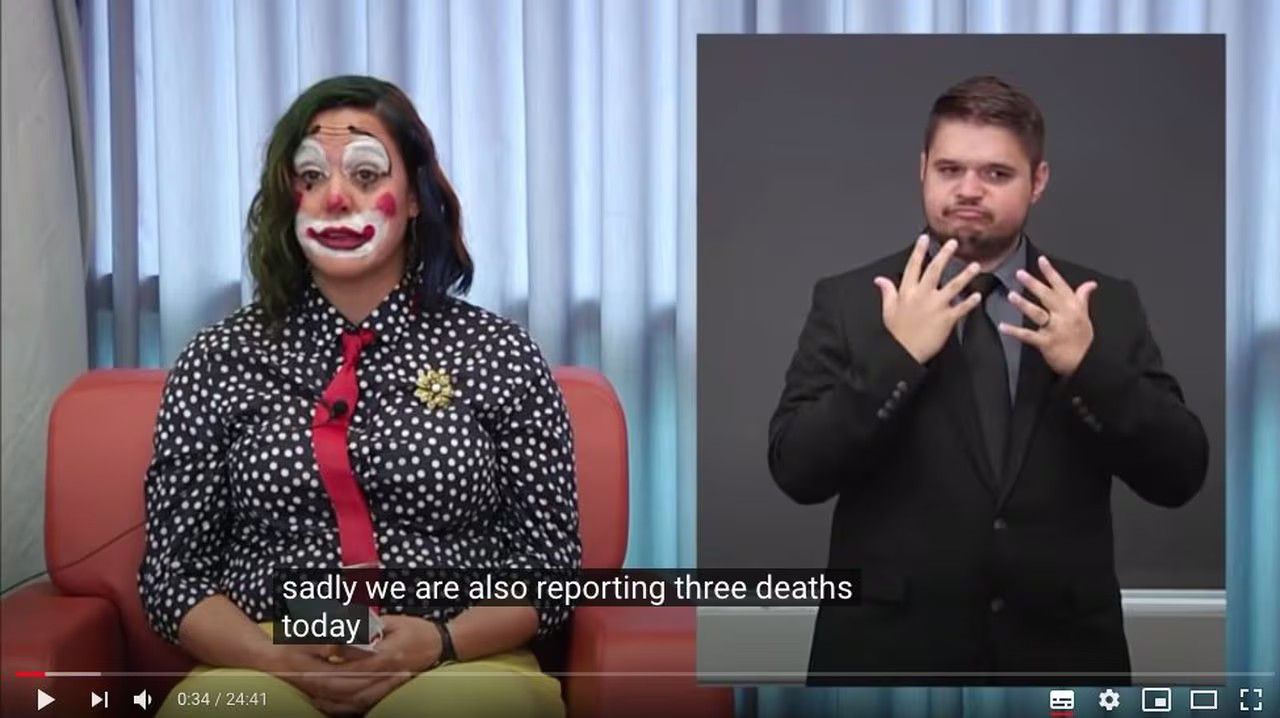 Oregen Public Health official on the left dressed as clown, sign language translator on the right making a face mid translation, closed caption " sadly we are also reporting 3 deaths today", circa October 30th 2020.
