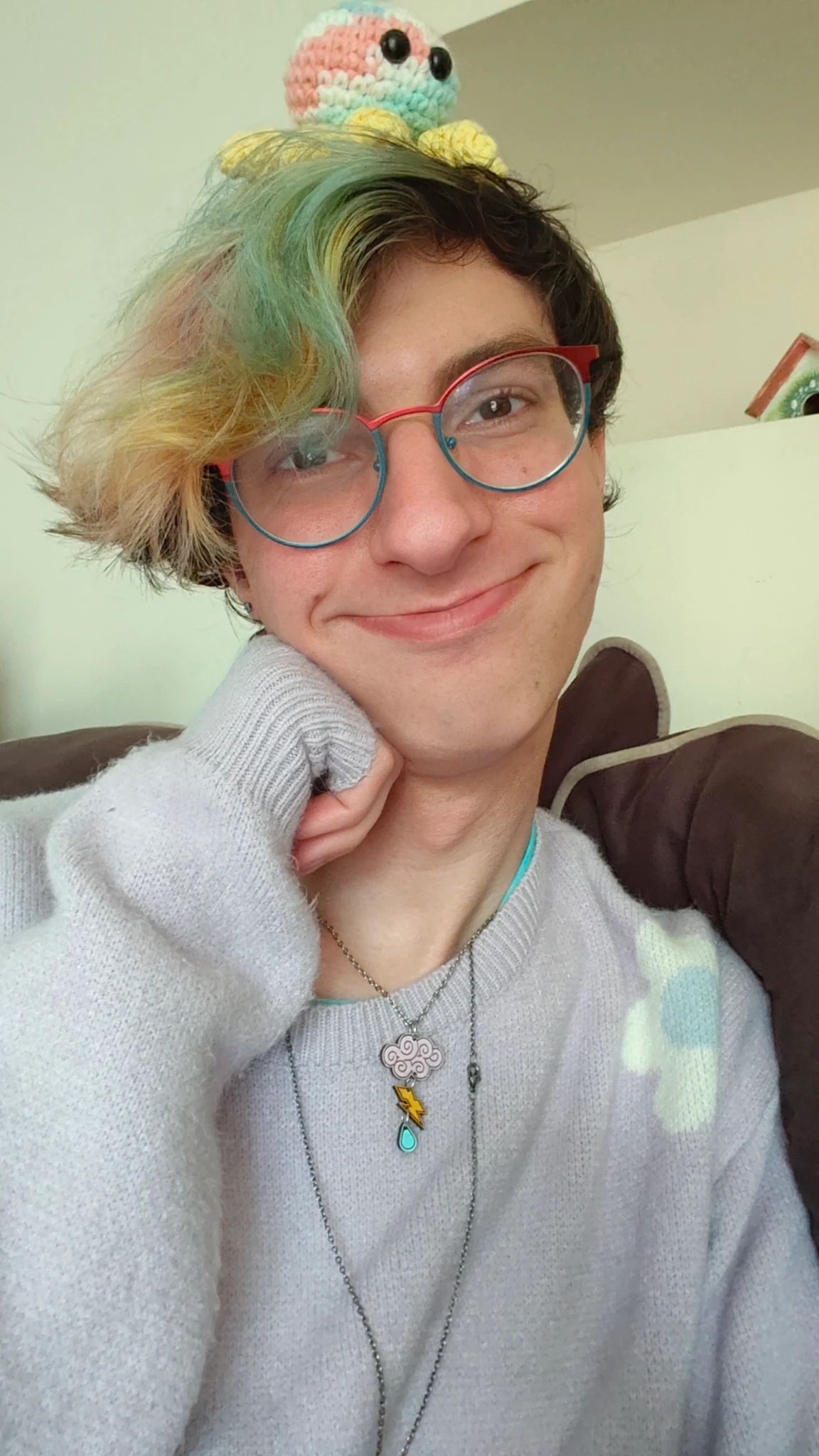 A girl with short rainbow hair and an octopus on her head.  She's wearing a lavender sweater with flowers on it and smiling.