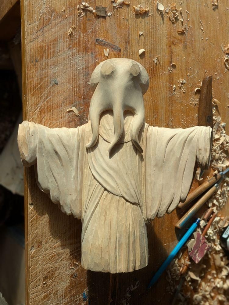 Draft of a woodcarved humanoid octopus wearing a dress / tunic cloth, arms wide open. On a workbench, woodships and tools beside the carving
