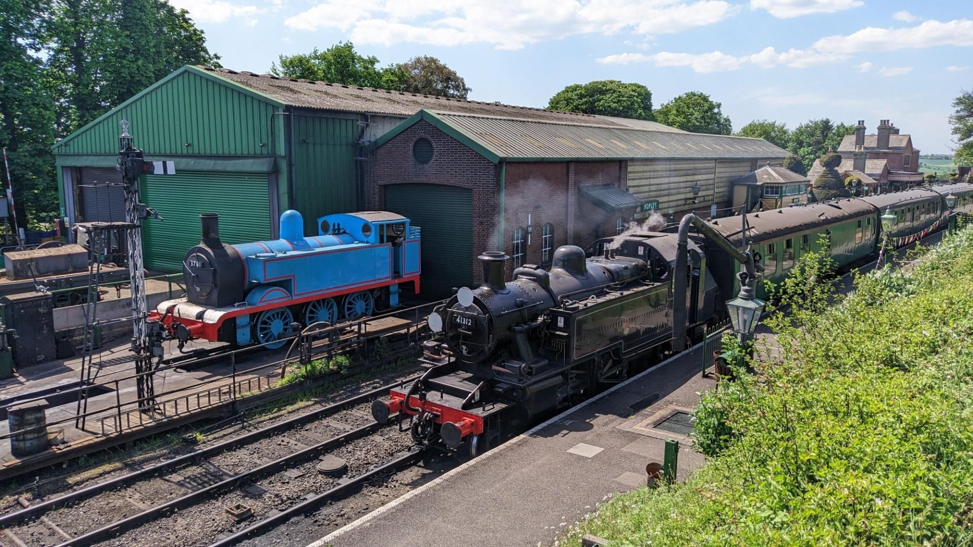 Steam loco is refilling water, behind the shed with a blue steam loco