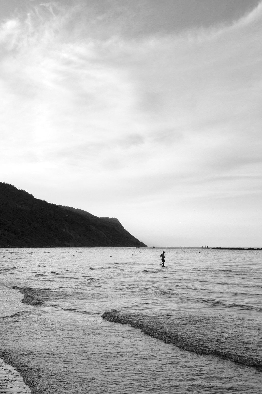 Black and white photo of a lone figure walking in the sea.