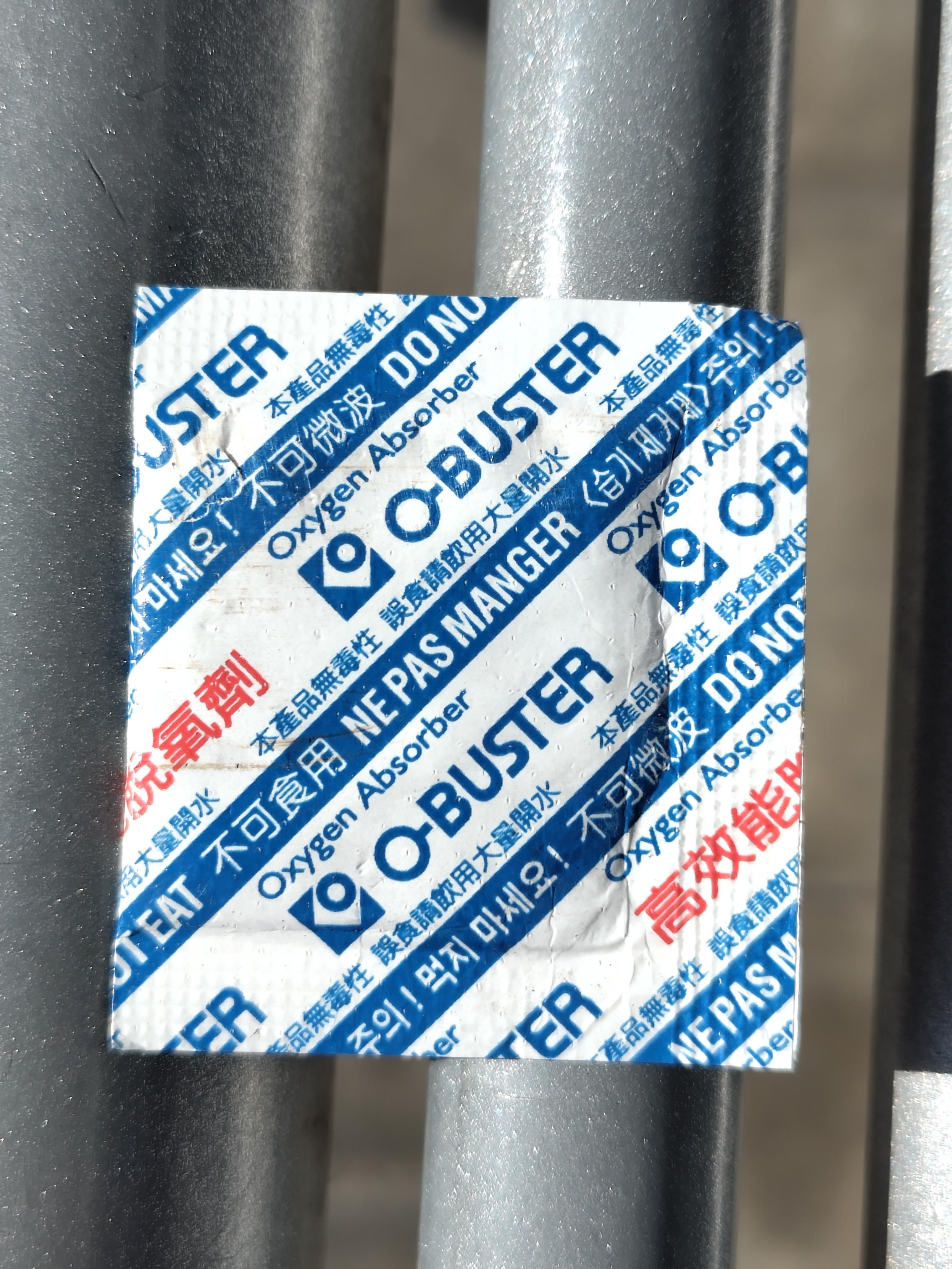 A small plastic folder that looks like those used for bandaids. 
It's almost square, 4 cm size and flat. It's white.
There are writings and signs in a diagonal arrangement, which are blue on white and read

Oxygen Absorber O-BUSTER A Chinese writing in red is on the same white stripe. 
 
A blue stripe is repeated a few times with white writings:

Ne pas manger. Do not eat (and probably the same phrase in Korean and Japanese... I think). 