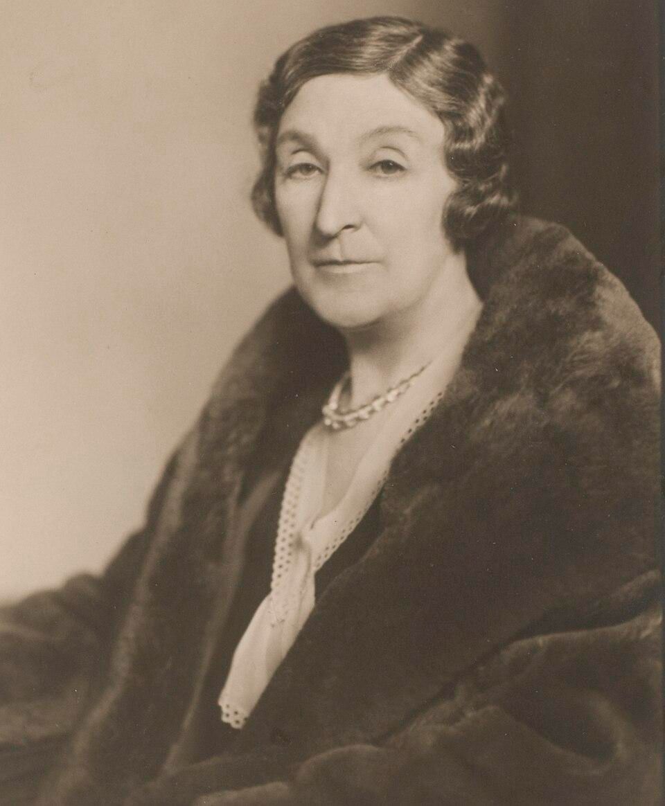 Ethel Florence Lindesay Richardson ('Henry Handel Richardson'), ca. 1935.

Elliott & Fry - State Library of NSW P1/1477

The photograph shows Richardson as a mature woman, turned slightly toward the camera in a three-quarter view. She gazes directly at the viewer with a calm expression.

Richardson has distinctive wavy hair styled in the fashion of the 1930s, with gentle finger waves framing her face. 

A luxurious dark fur coat or stole draped over her shoulders.

A light-colored blouse or dress with delicate lace or eyelet detailing along the neckline and front.

A pearl necklace that adds refinement to the ensemble

https://en.wikipedia.org/wiki/Henry_Handel_Richardson#/media/File:Henry_(ethel)_Richardson_SLNSW_FL3290825.jpg