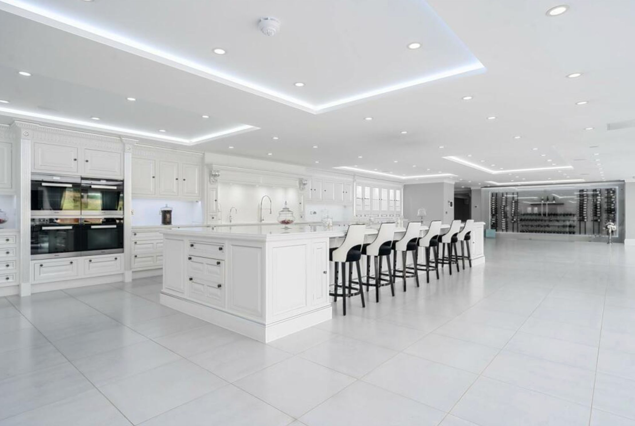 A large white kitchen in a huge open plan room with white tiles. There is an inordinate amount of empty space. 