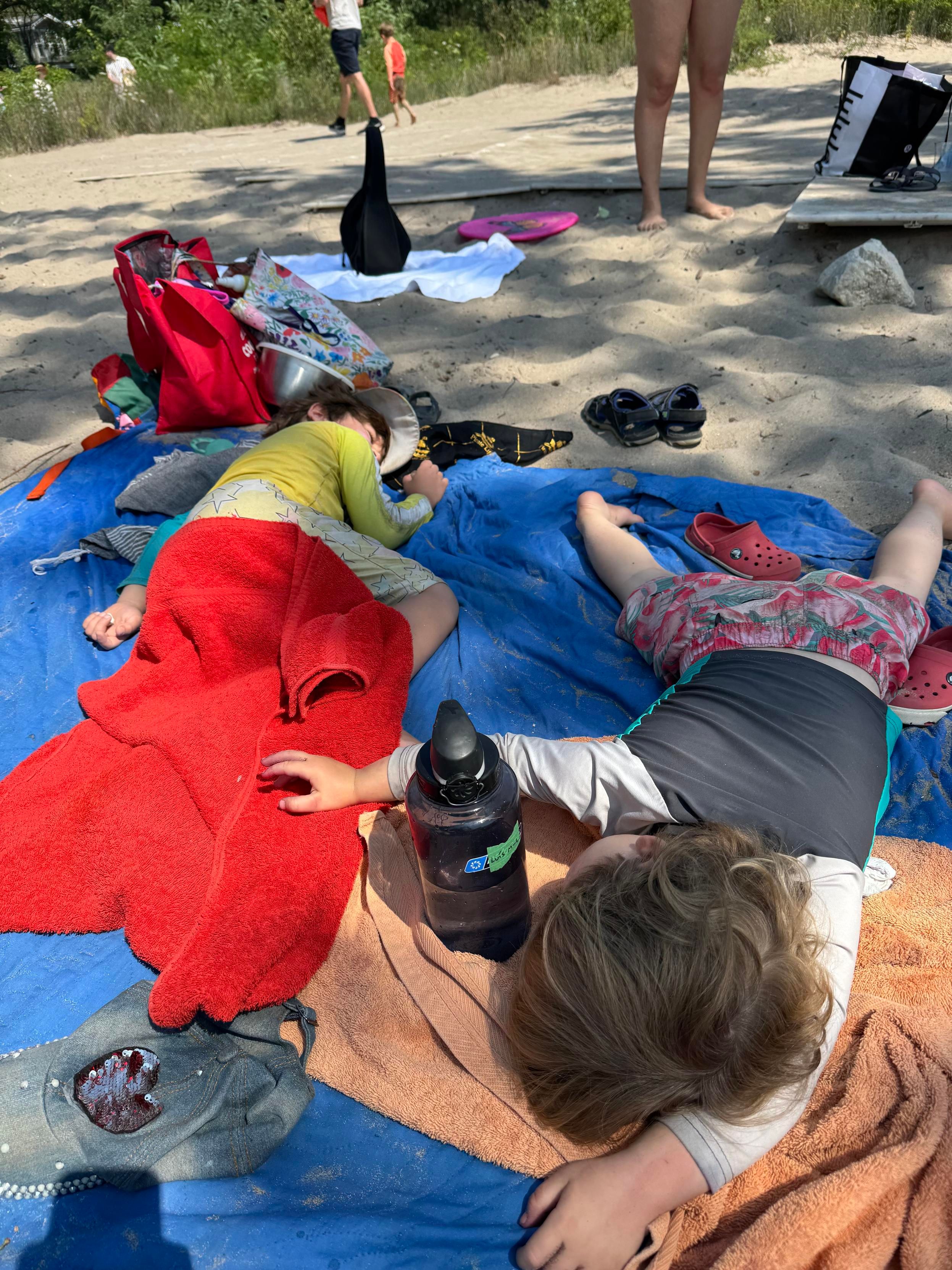 two tired children lying on a picnic blanket on the sand