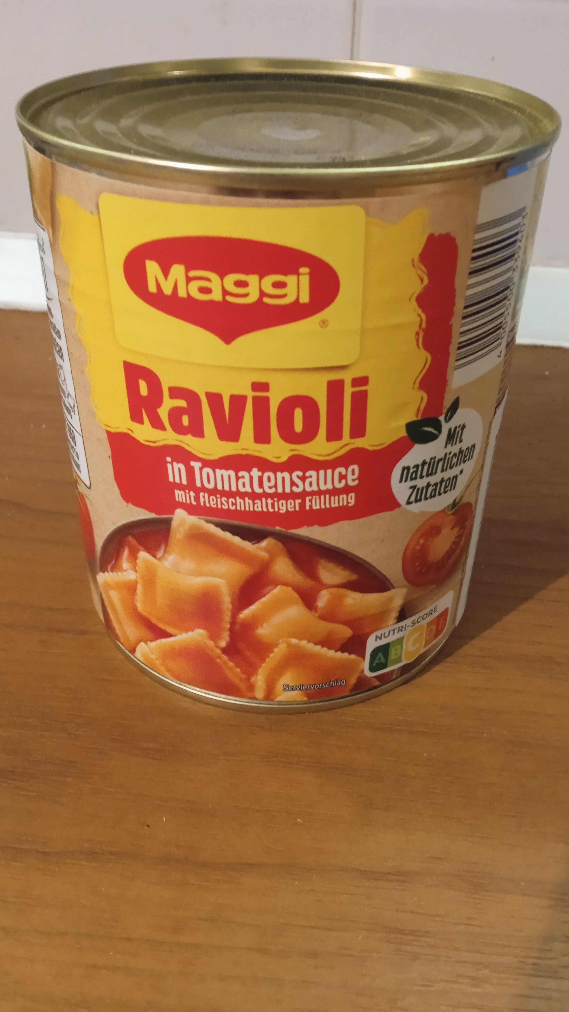 On a light brown table, a can of industrial ravioli in tomato sauce, Maggi brand.