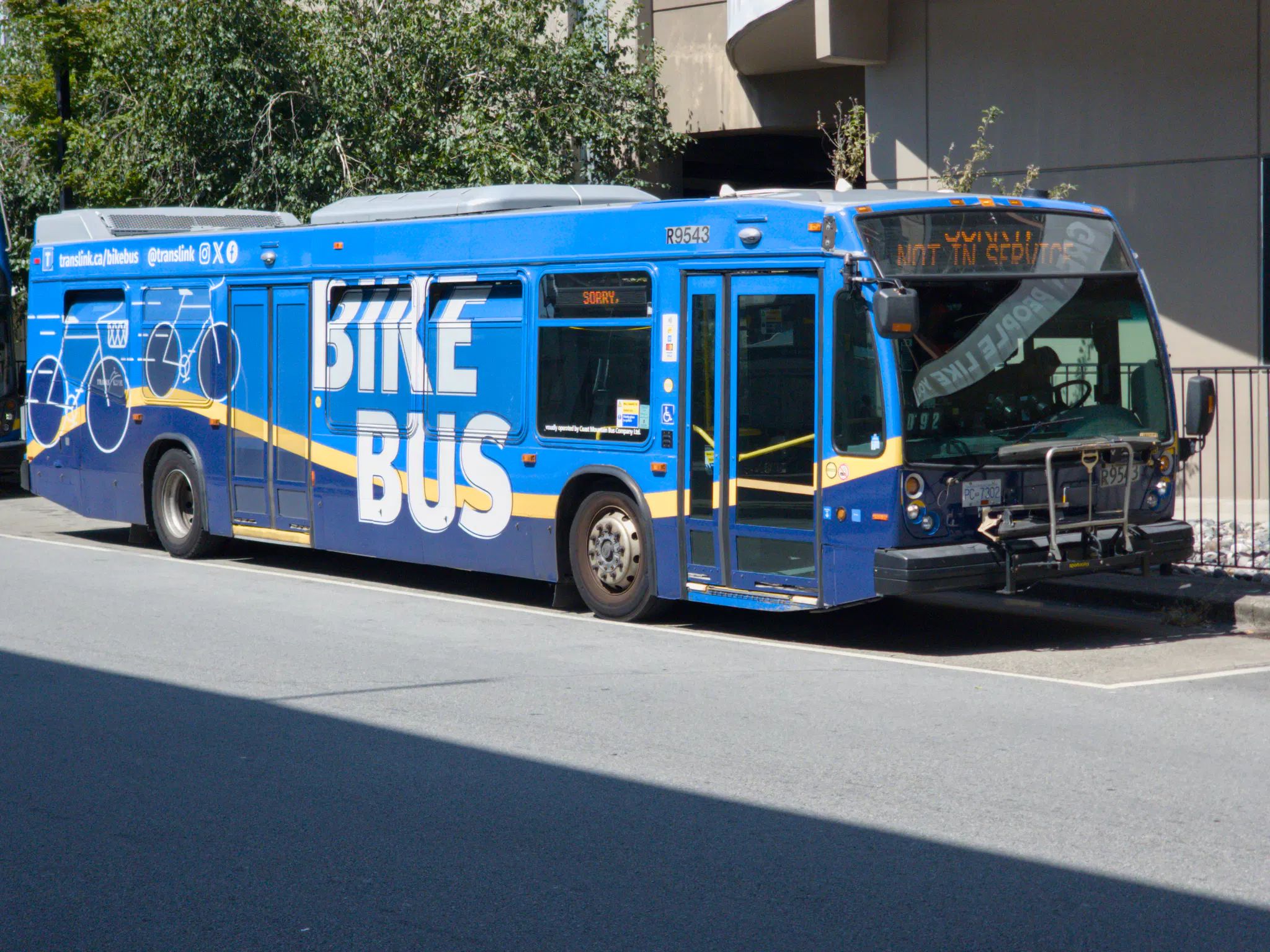 One of TransLink's Bike Buses, a 2009 Nova LFS which is internally fitted with bike racks. It has a blue Bike Bus livery that also covers most of the windows, with pictograms of bikes at the back and the words "BIKE BUS" in big letters in the middle.