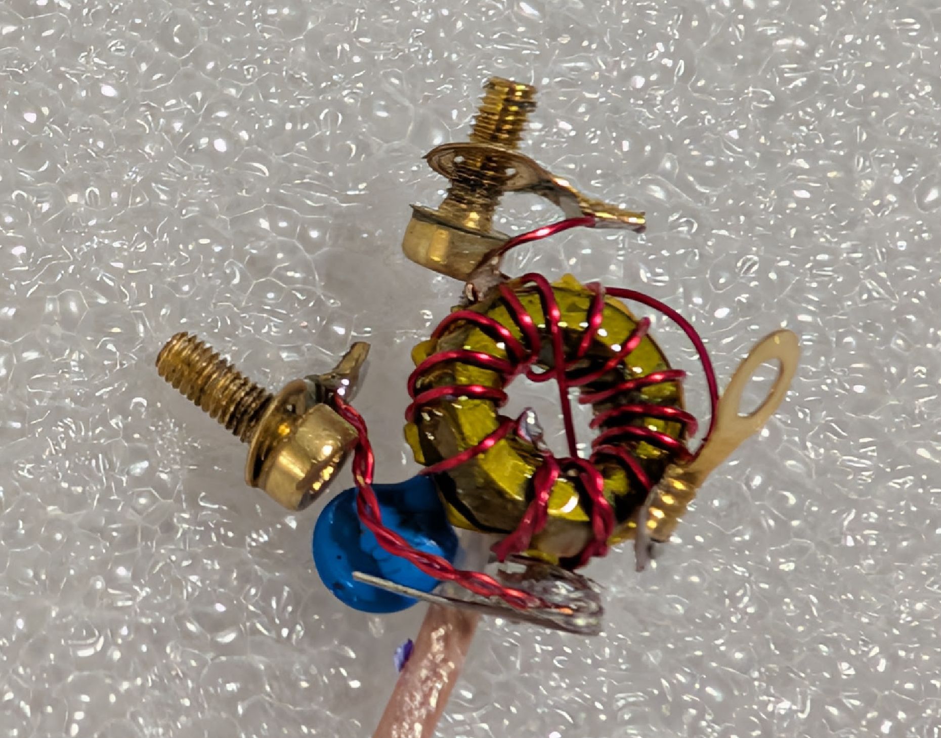 Electrical components removed from broken box: a tapped autotransformer with three ring terminals at the connections, and a blue high-voltage capacitor. Two of the three ring terminals have brass M3x8 screws currently installed. 1/10" RG316 is visible at the bottom.