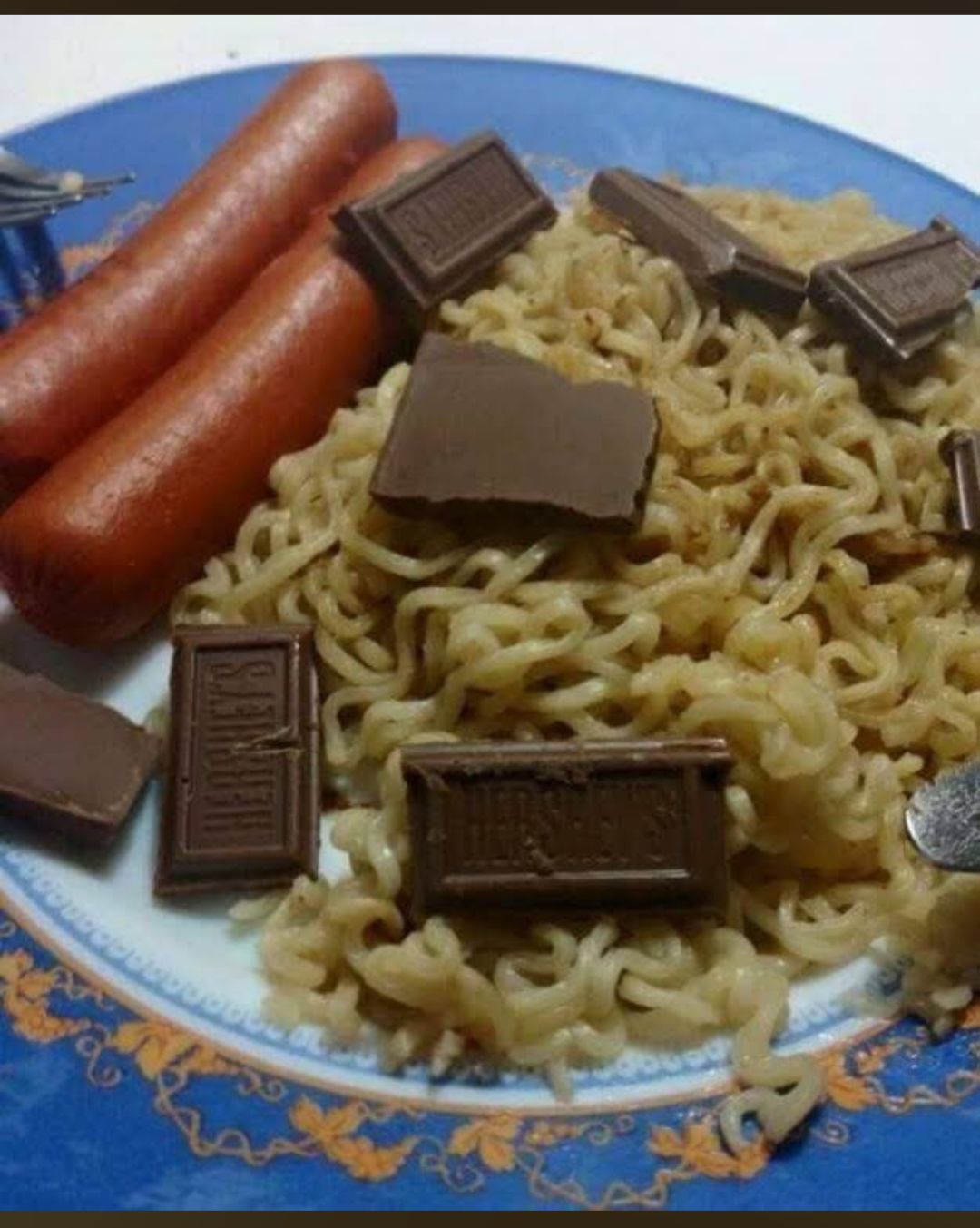 A photo of a plate of instant noodles, sausages, and pieces of what looks like dark chocolate. I'm very confused. 