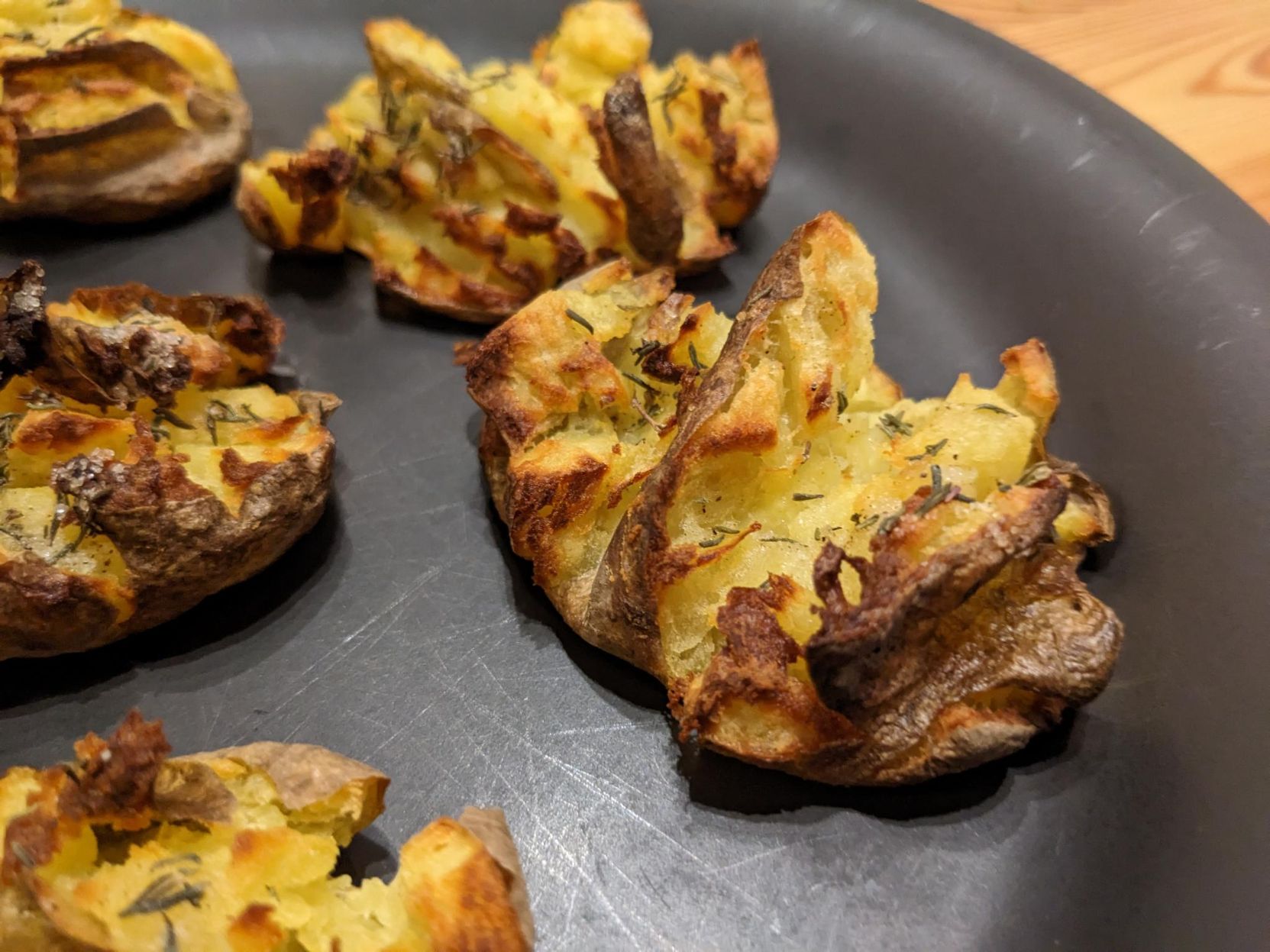 Smashed, roasted potatoes on a plate. They look very crispy.