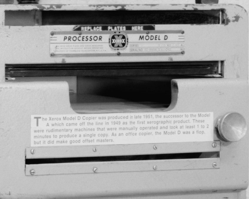 The Xerox Model D copier, introduced in 1951.

The photograph shows:
The Xerox Processor Model D machine with its distinctive labeling
"REPLACE PLATES HERE" instruction visible at the top
The machine's simple, boxy design characteristic of early 1950s office equipment
An explanatory placard below describing the machine's history and function

https://www.loc.gov/pictures/item/oh1541.photos.126771p