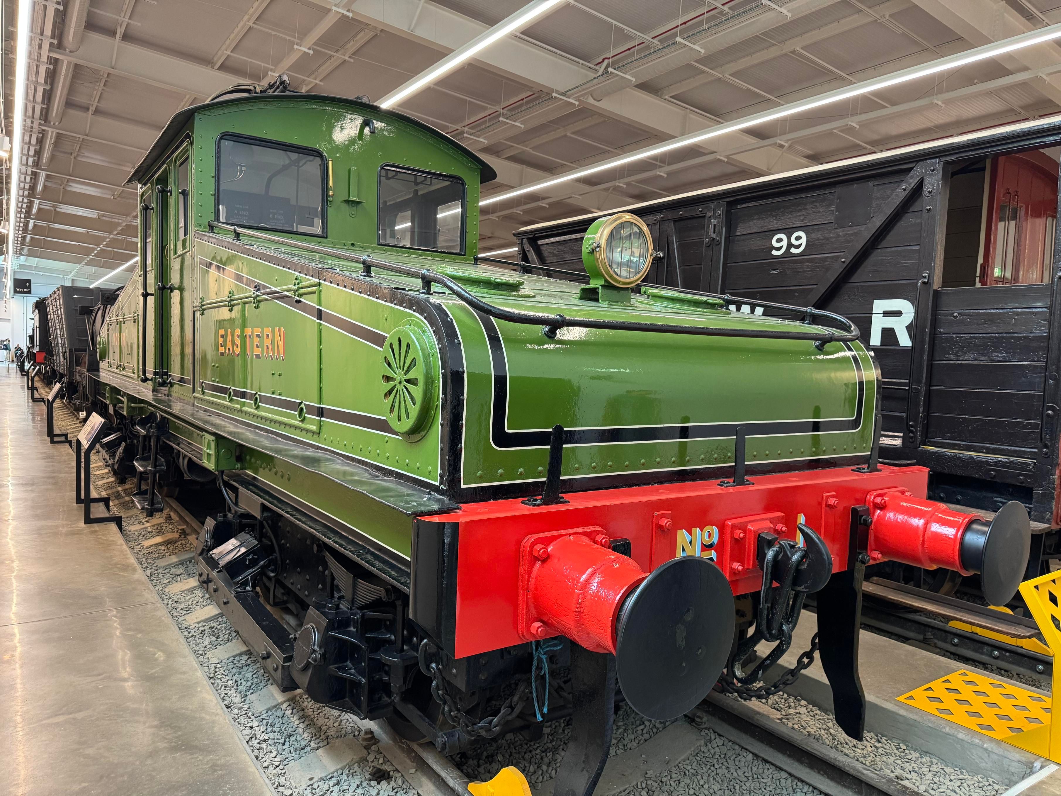 A three quarters view of a green electric locomotive its red numbers and black highlights. There is a large headlamp on the front and a low, sloped profile leading up to the centre cabin. On the side “North Eastern” is written in yellow