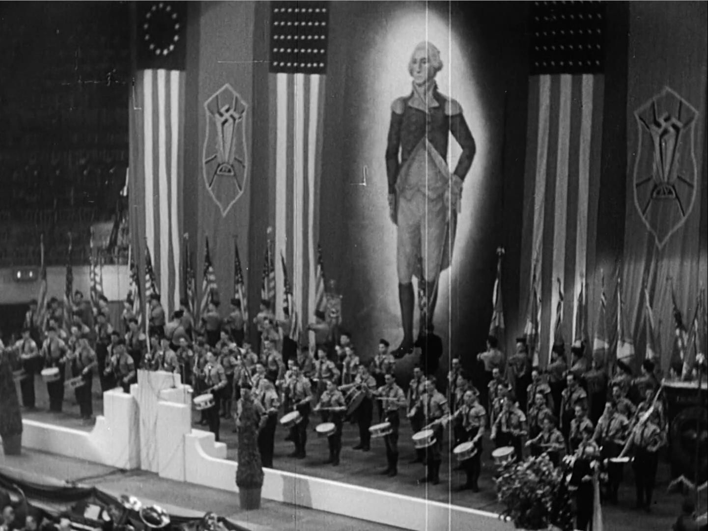 Photo of the stage at the 1939 German-American Bund rally at Madison Square Garden, with a large portrait of George Washington flanked by American flag banners and swastikas, with a band on the stage dressed in Nazi uniforms.