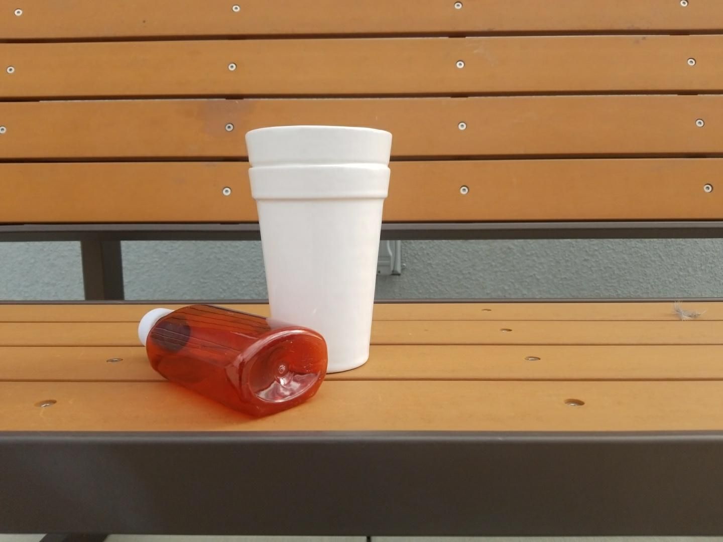 A white 3D-printed facsimile of stacked foam cups on a bench next to an empty cough syrup bottle.
