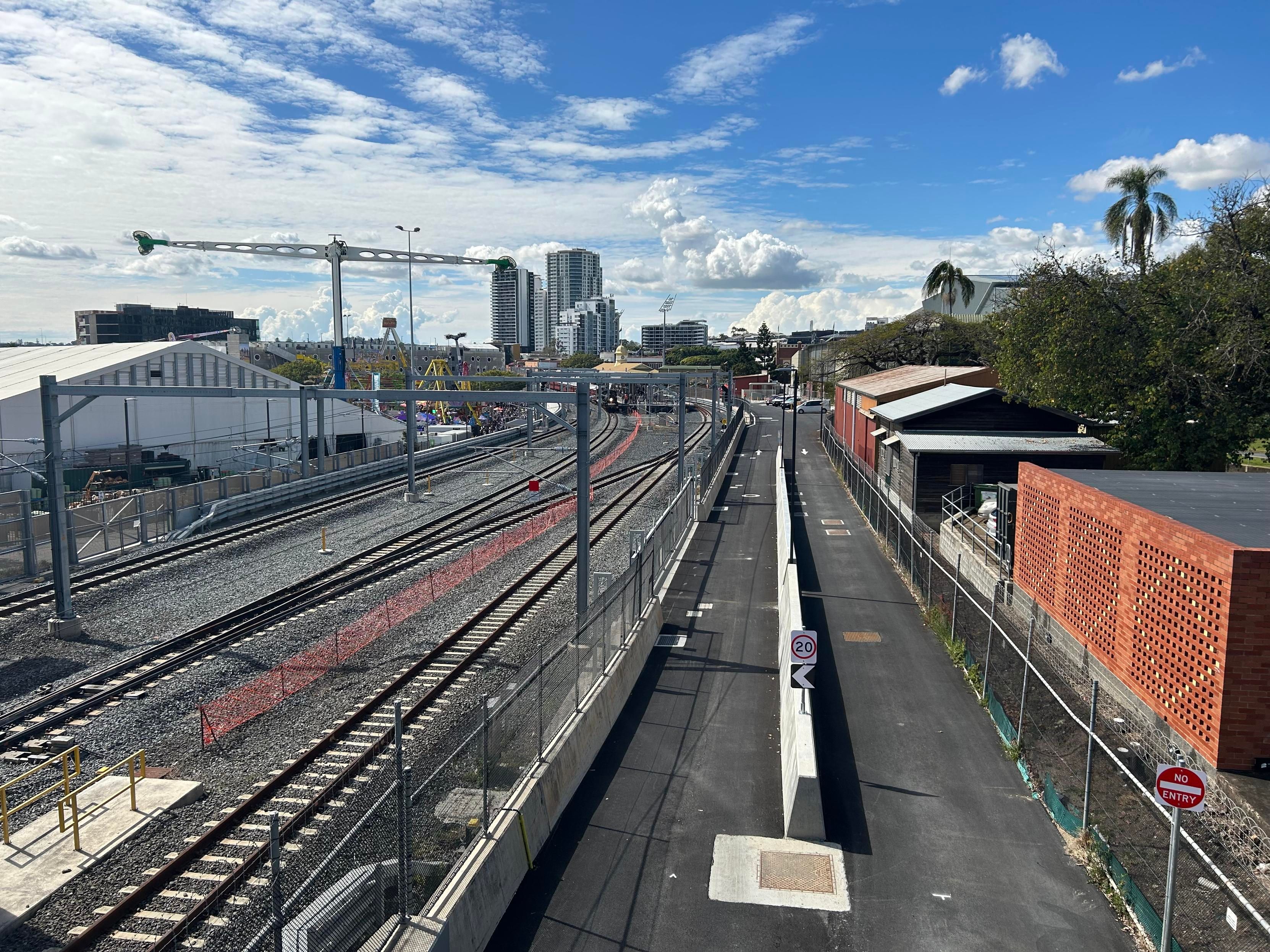 Photo taken of a green steam train standing at the station in the Brisbane exhibition grounds, the rides and pavilions of the show can be seen surrounding the tracks.